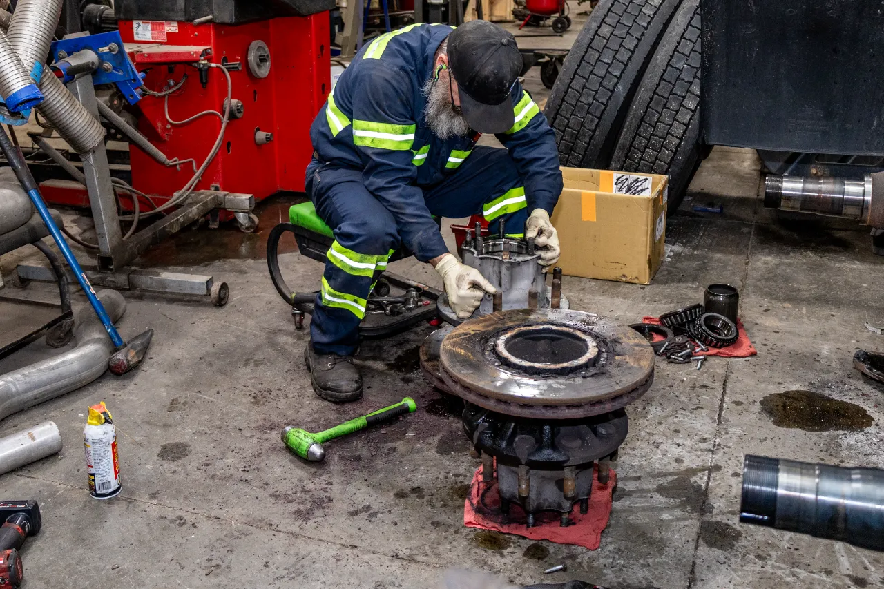 Heavy-duty brake service, technician removing drum assembly and bearings on shop floor.