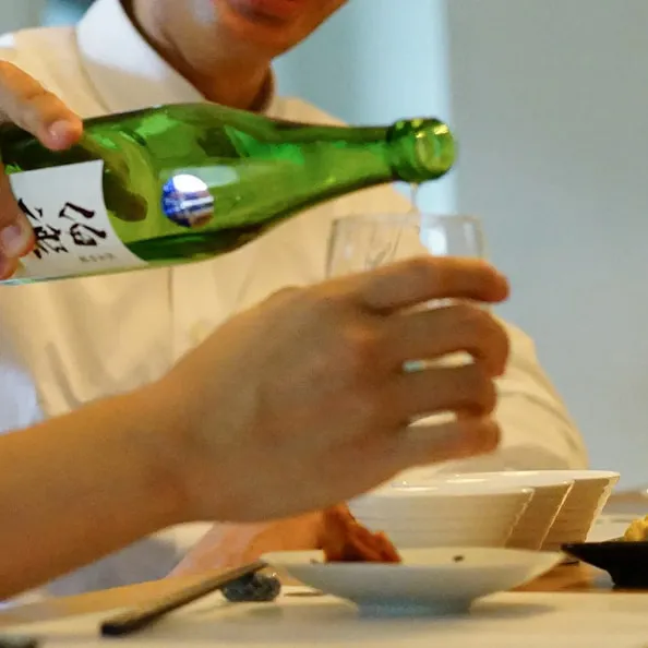 Pouring a drink into a glass in front of a table.