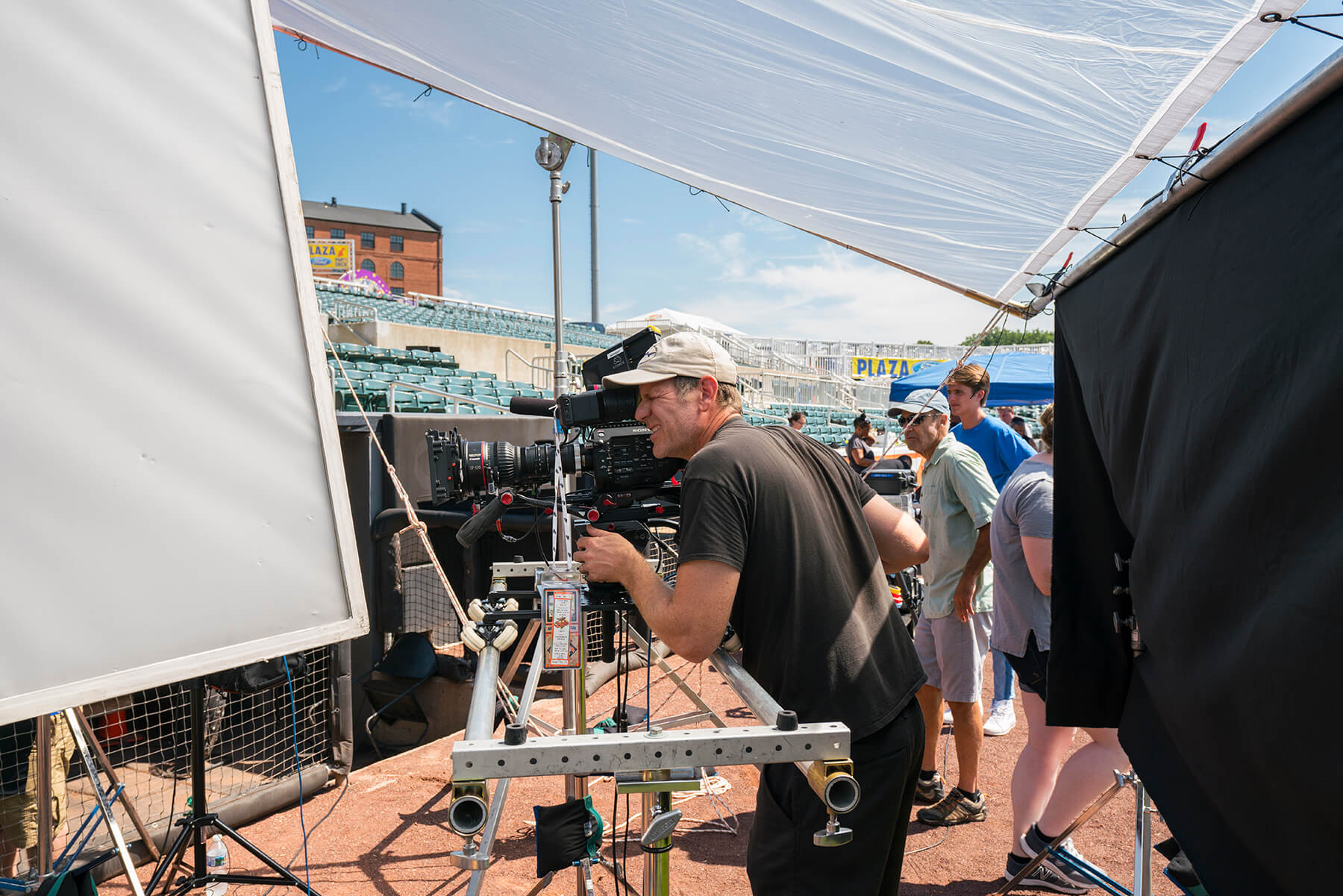 Camera operator filming under large diffusion frames on an outdoor set with crew nearby