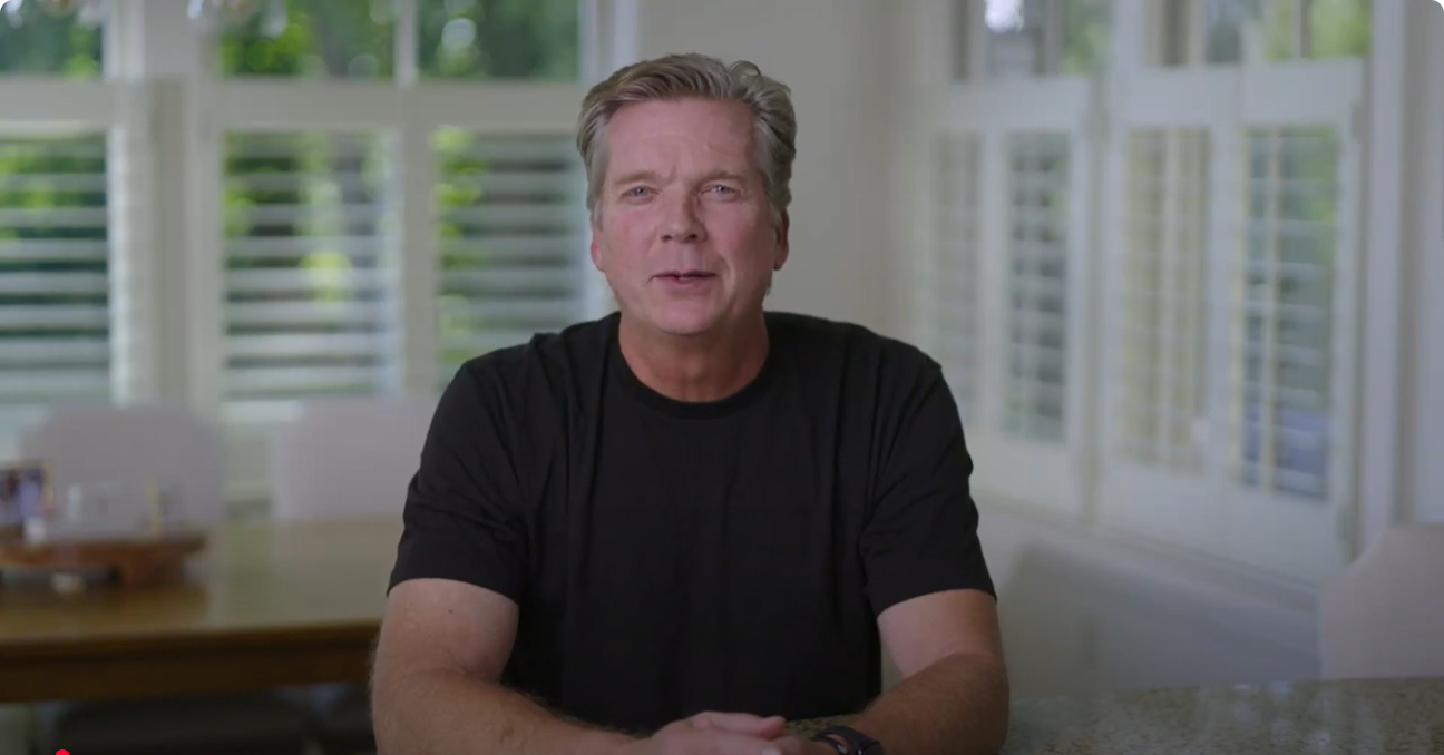 Patrick Rafferty in a black T-shirt seated at a table and speaking to camera, kicking off his weekly video series