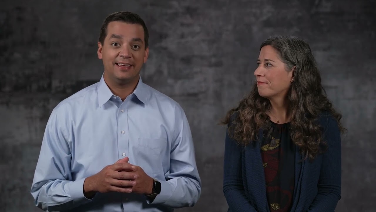 Man in a light blue shirt and a woman with long curly hair presenting side by side against a dark gray backdrop