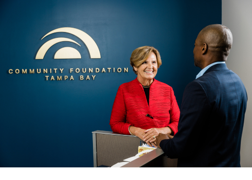 Woman and man standing in front of Community Foundation logo on a wall