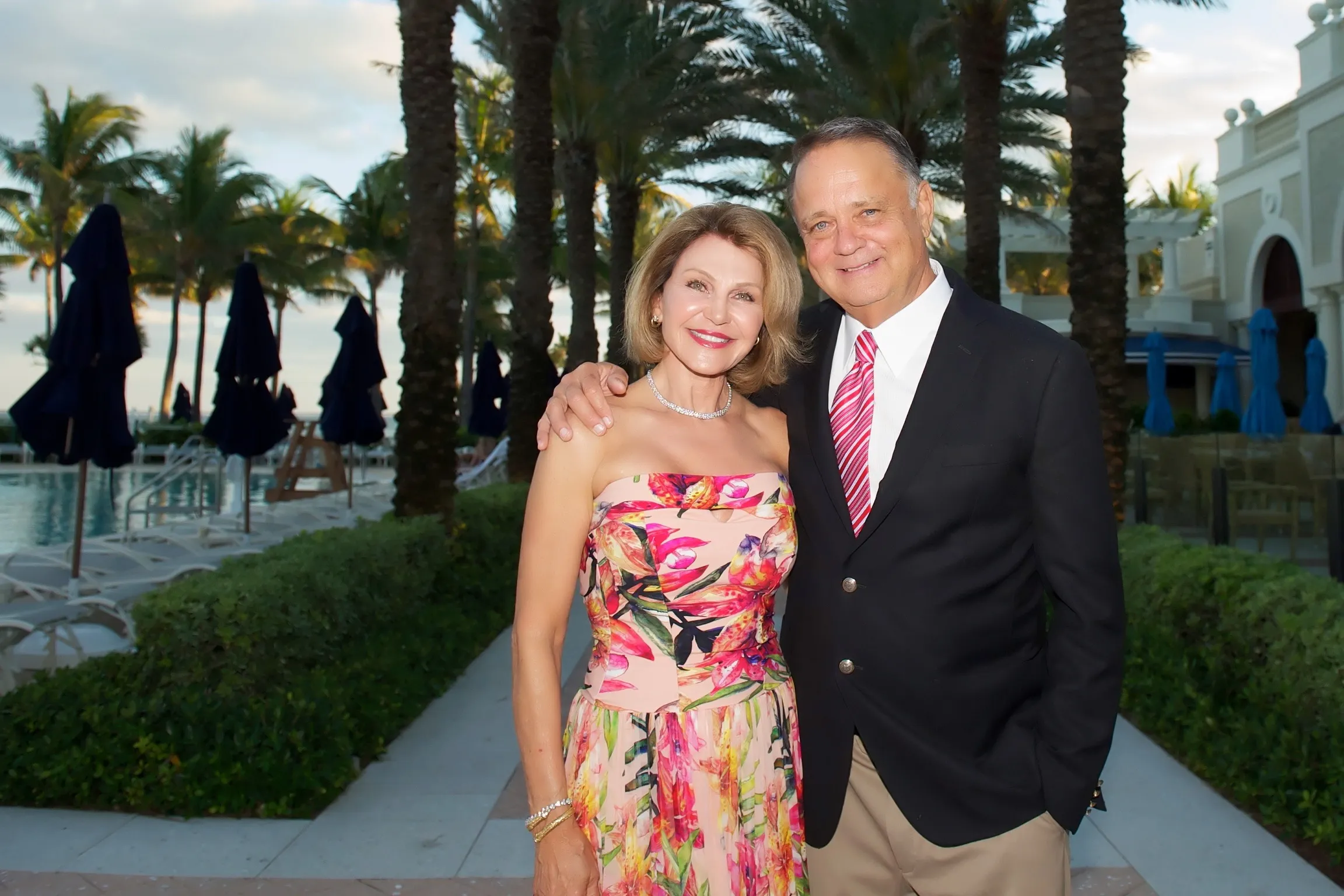 A man and woman smiling together outdoors at a tropical resort