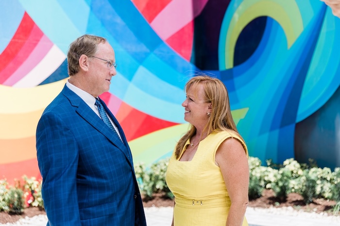 Man and a women dressed professionally standing in front of a bright mural talking