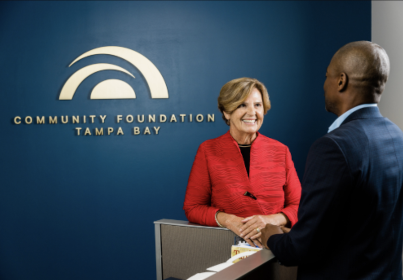 Woman and man standing in front of Community Foundation logo on a wall