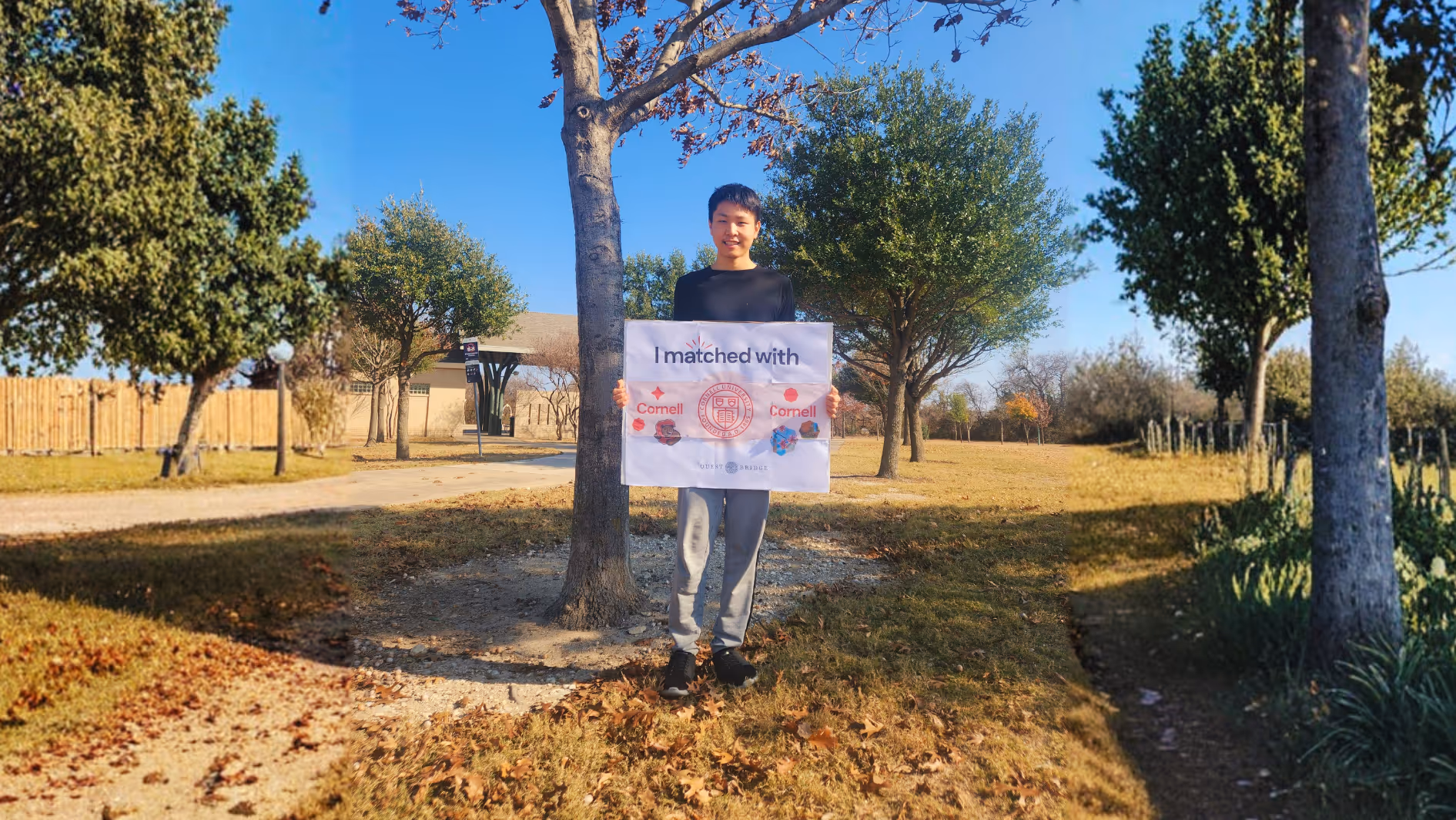 A wide shot of a student outdoors in a park holding a "I matched with Cornell" sign, surrounded by oak trees and autumn leaves on a sunny day.