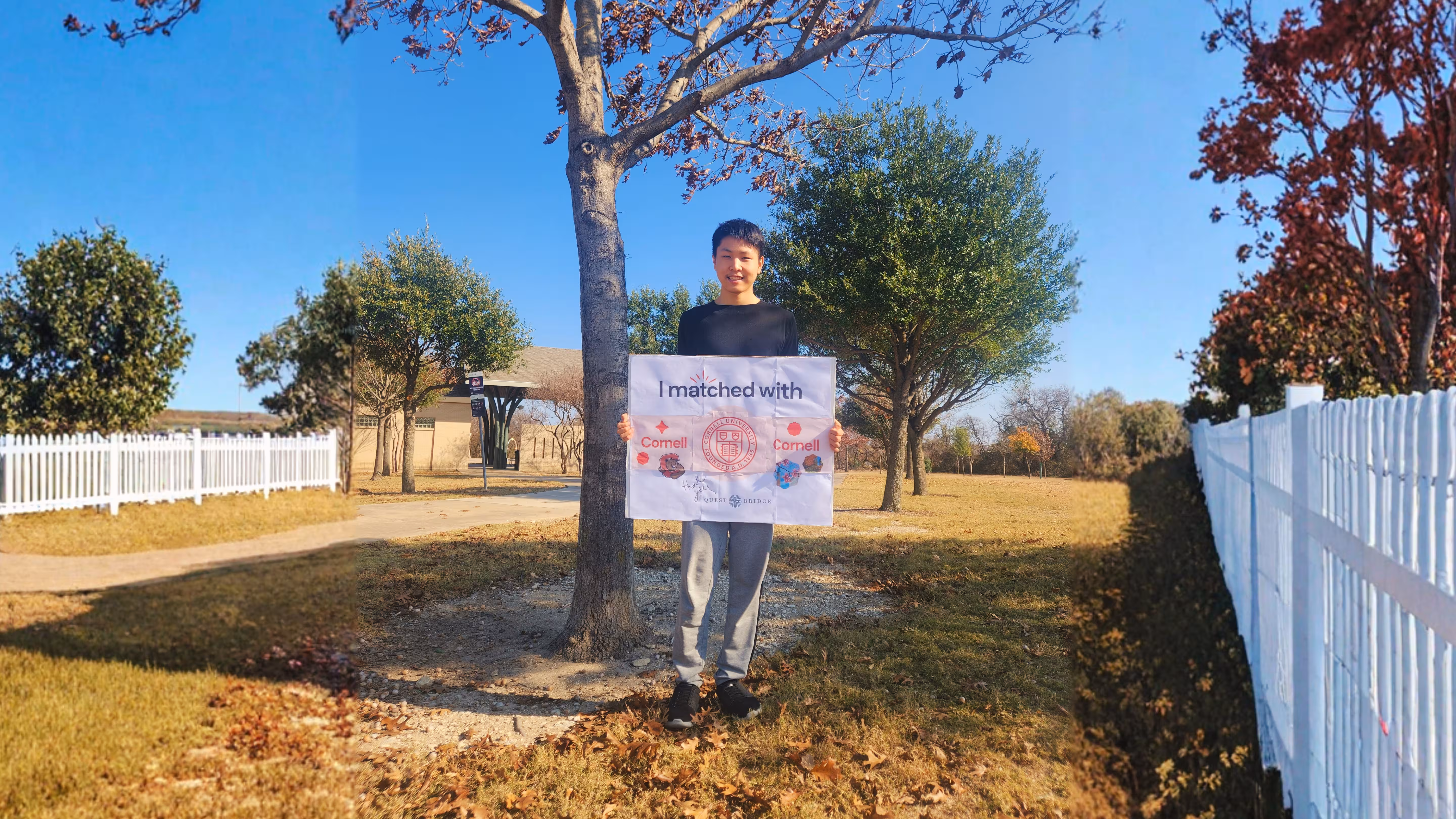 A wide shot of a student outdoors in a park holding a "I matched with Cornell" sign, surrounded by oak trees and autumn leaves on a sunny day.