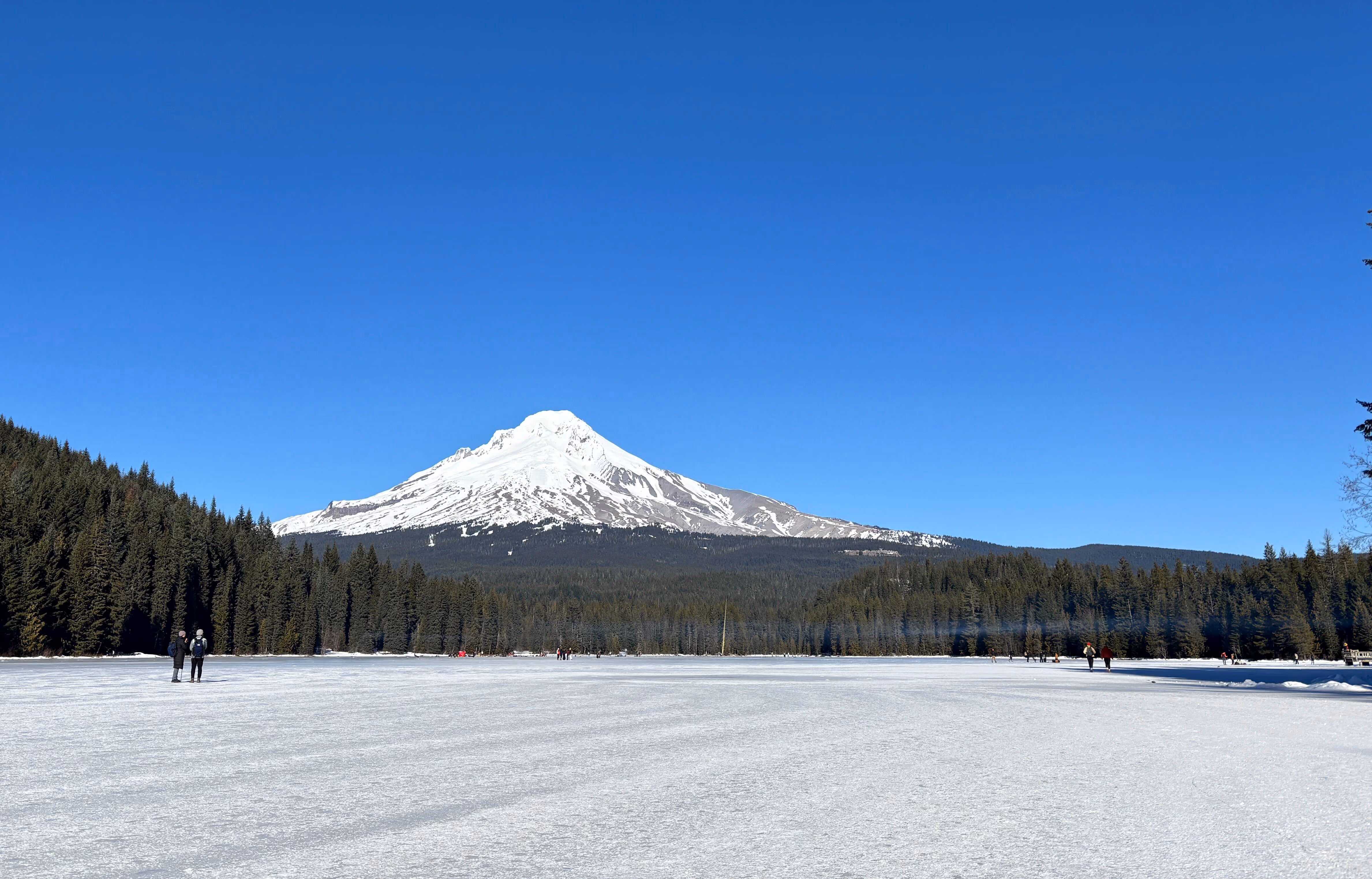 Hikers walk across a frozen Trillium Lake on a sunny, warm day near Mount Hood near Government Camp, Ore., on Jan. 24, 2026.