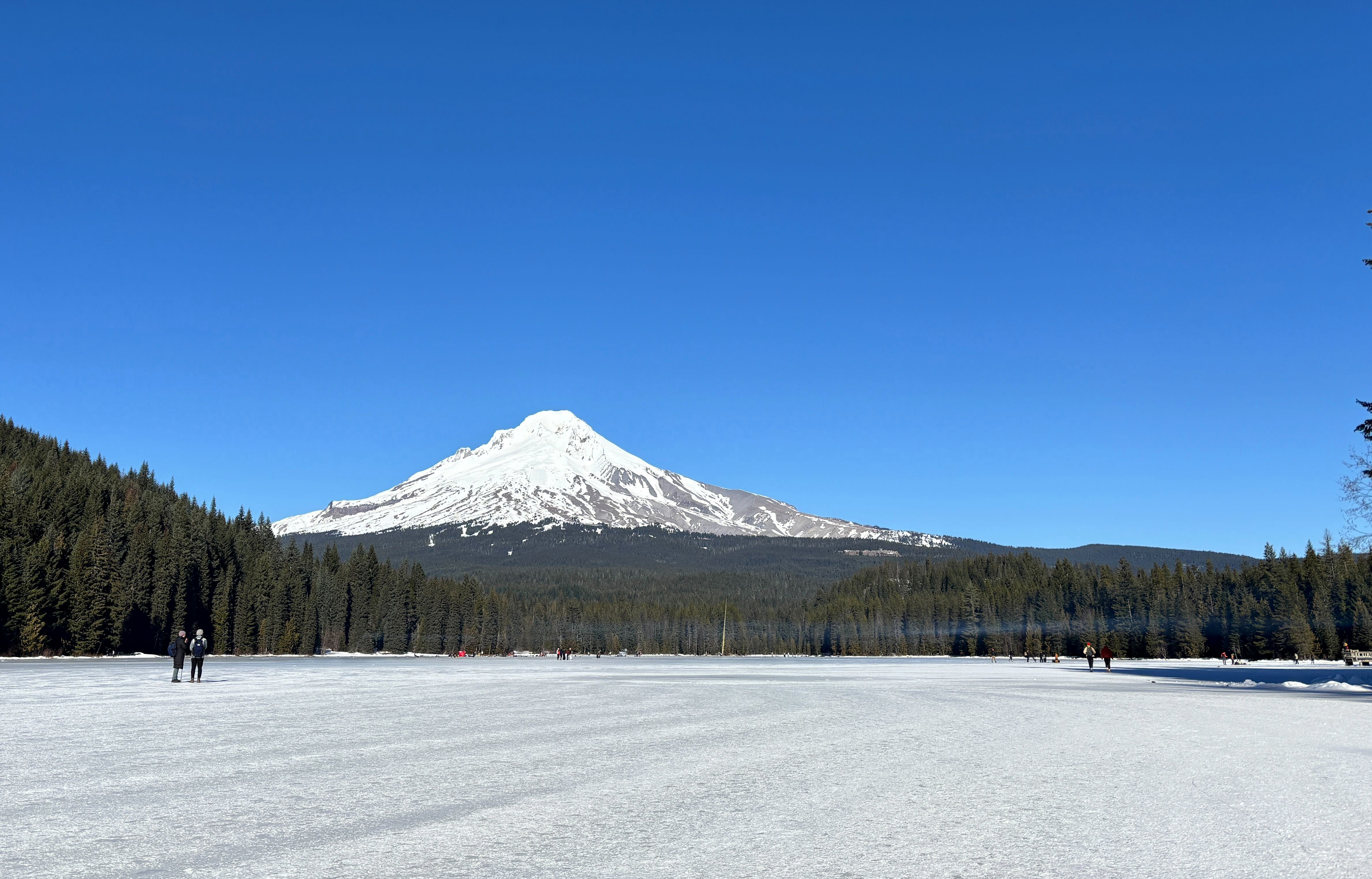 Hikers walk across a frozen Trillium Lake on a sunny, warm day near Mount Hood near Government Camp, Ore., on Jan. 24, 2026.