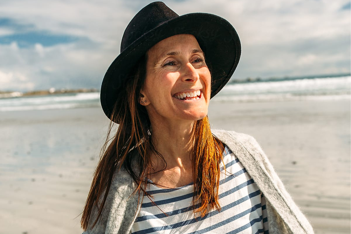 A woman smiles in the distance while walking on the beach