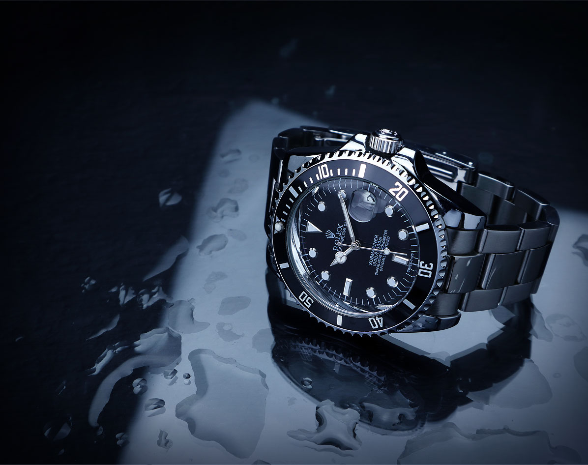 A premium watch with metal band resting on wet dark surface with water droplets.