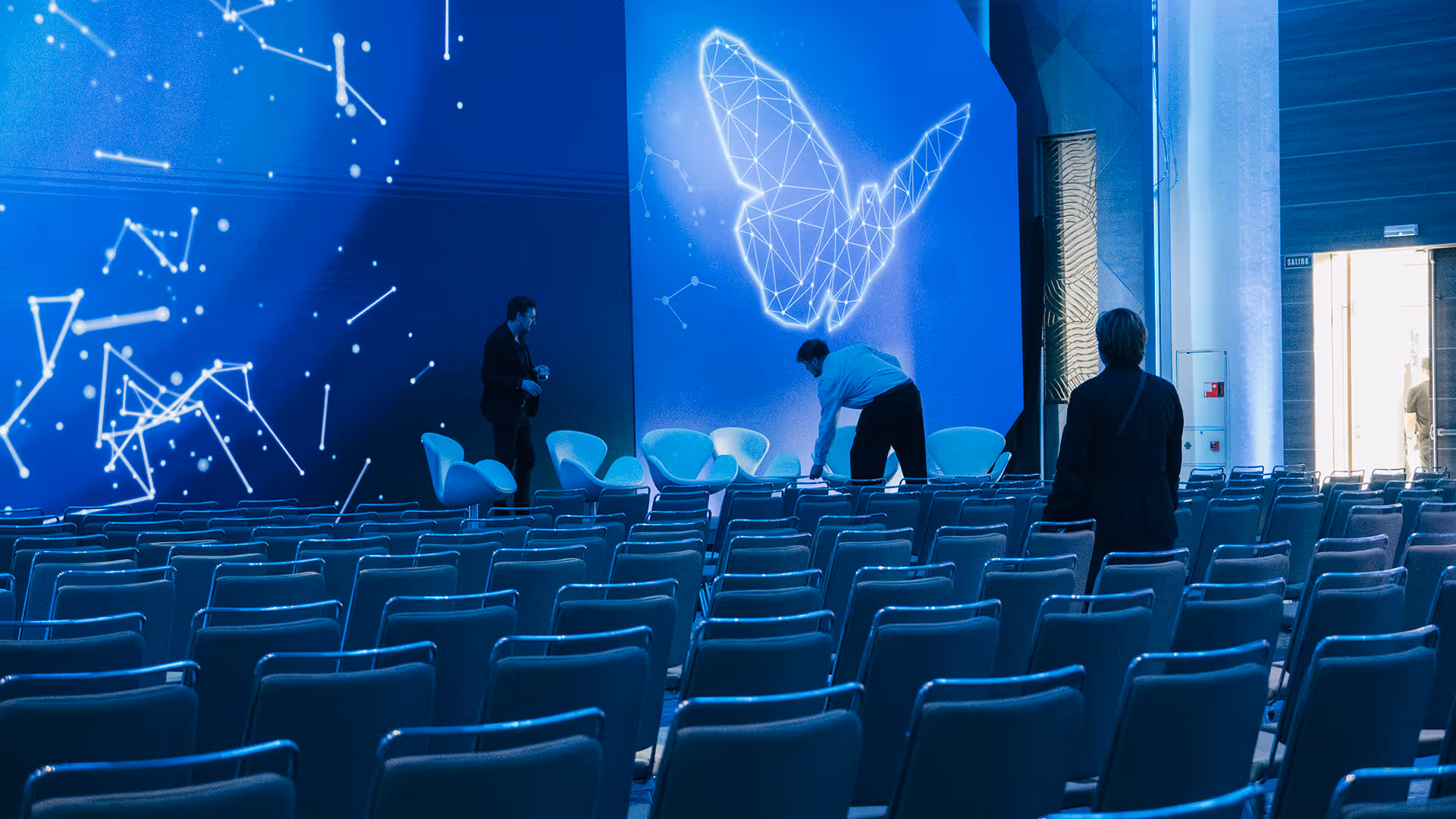 Event professionals finalising stage and seating arrangement for corporate meeting.