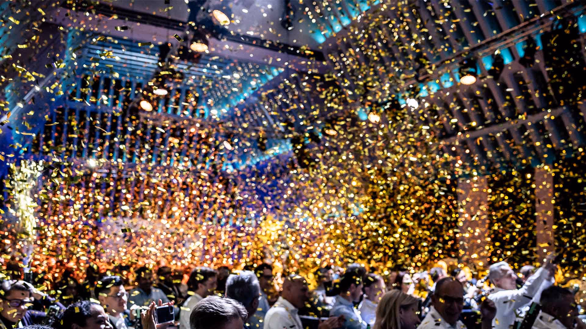 Gold confetti falling from ceiling onto corporate meeting participants.