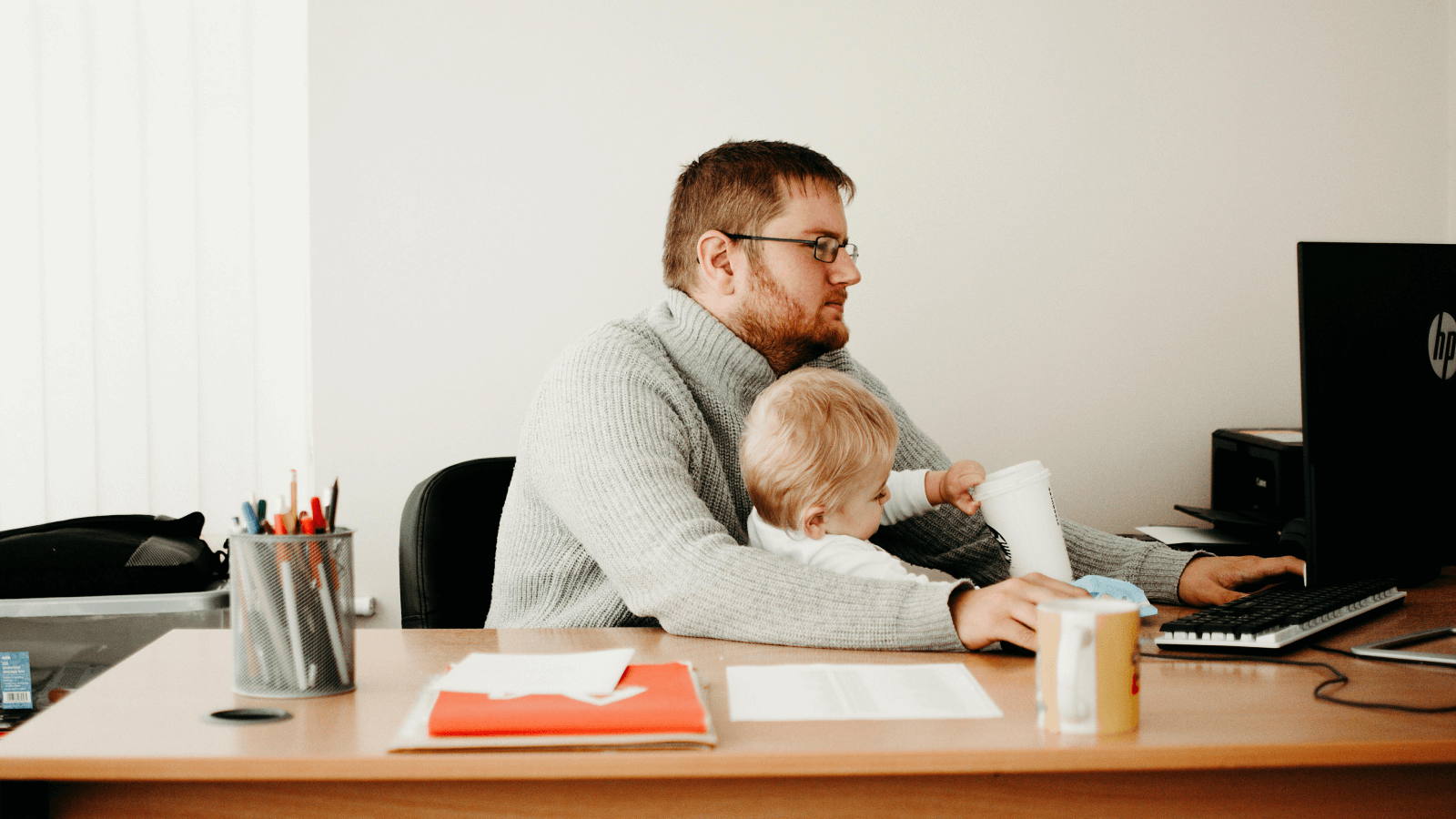 dad working at his desk with a child sat on his knee 