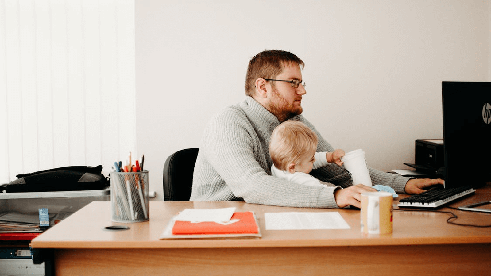Dad working from his home office with a toddler sat on his knee