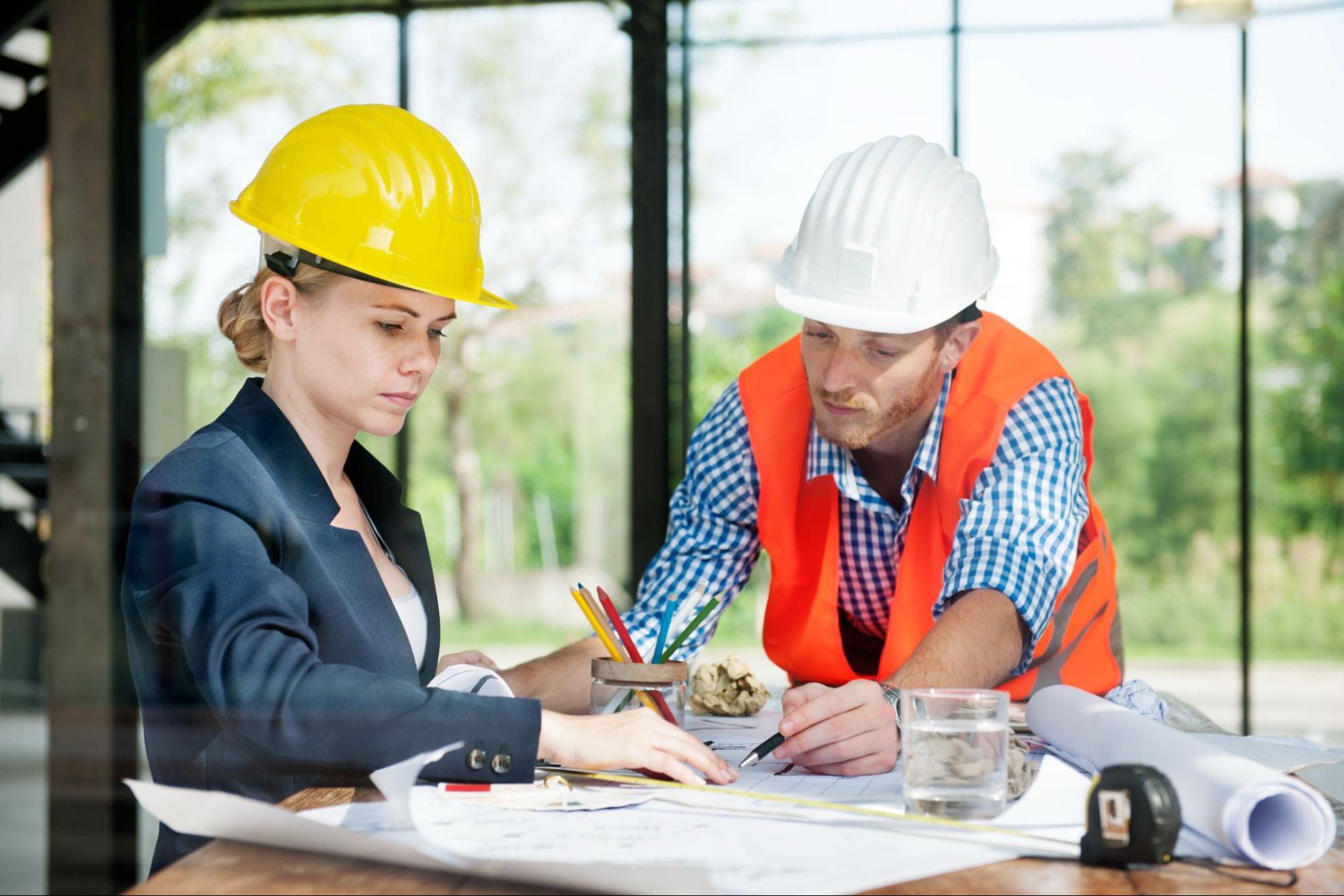 Two construction workers working on drawing up the construction plans.