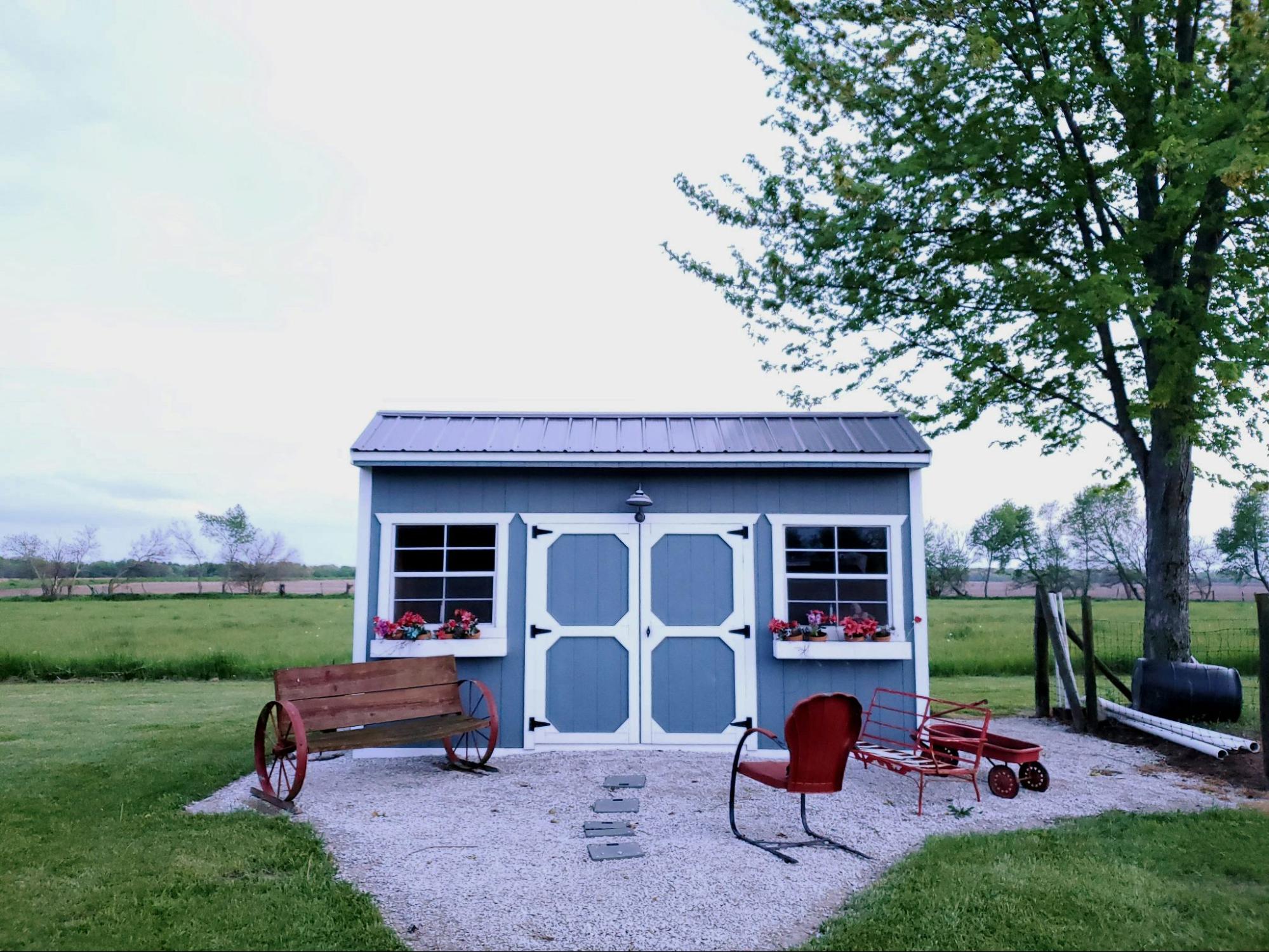 A wooden blue garden shed with seats in front.