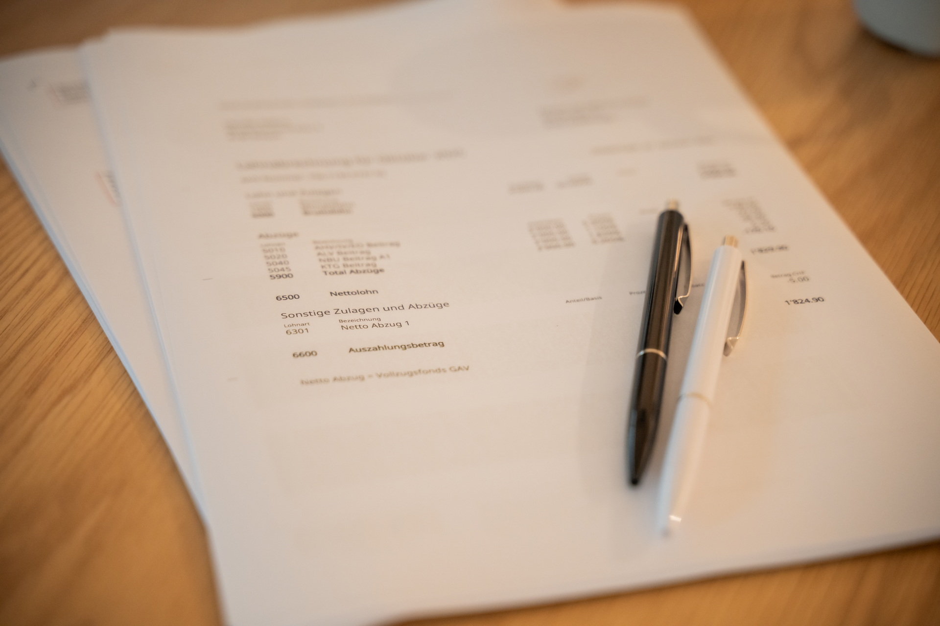 Zwei Kugelschreiber, einer schwarz und einer weiss, liegen auf mehreren Personalabrechnungsdokumenten auf einem Holztisch - ein Symbol für Lohnbuchhaltung und Personalwesen.