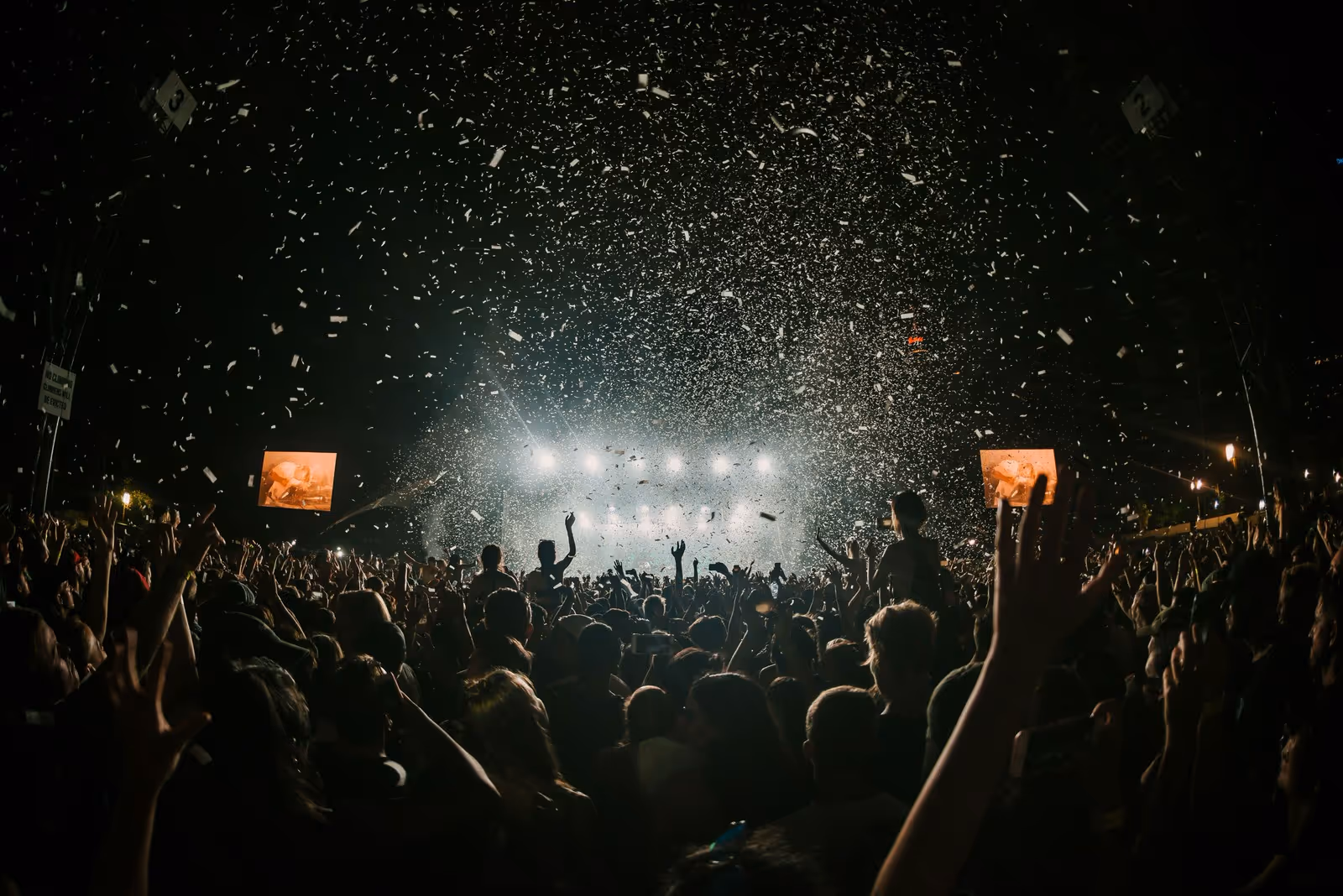 Crowd with arms in the air, facing a lit stage