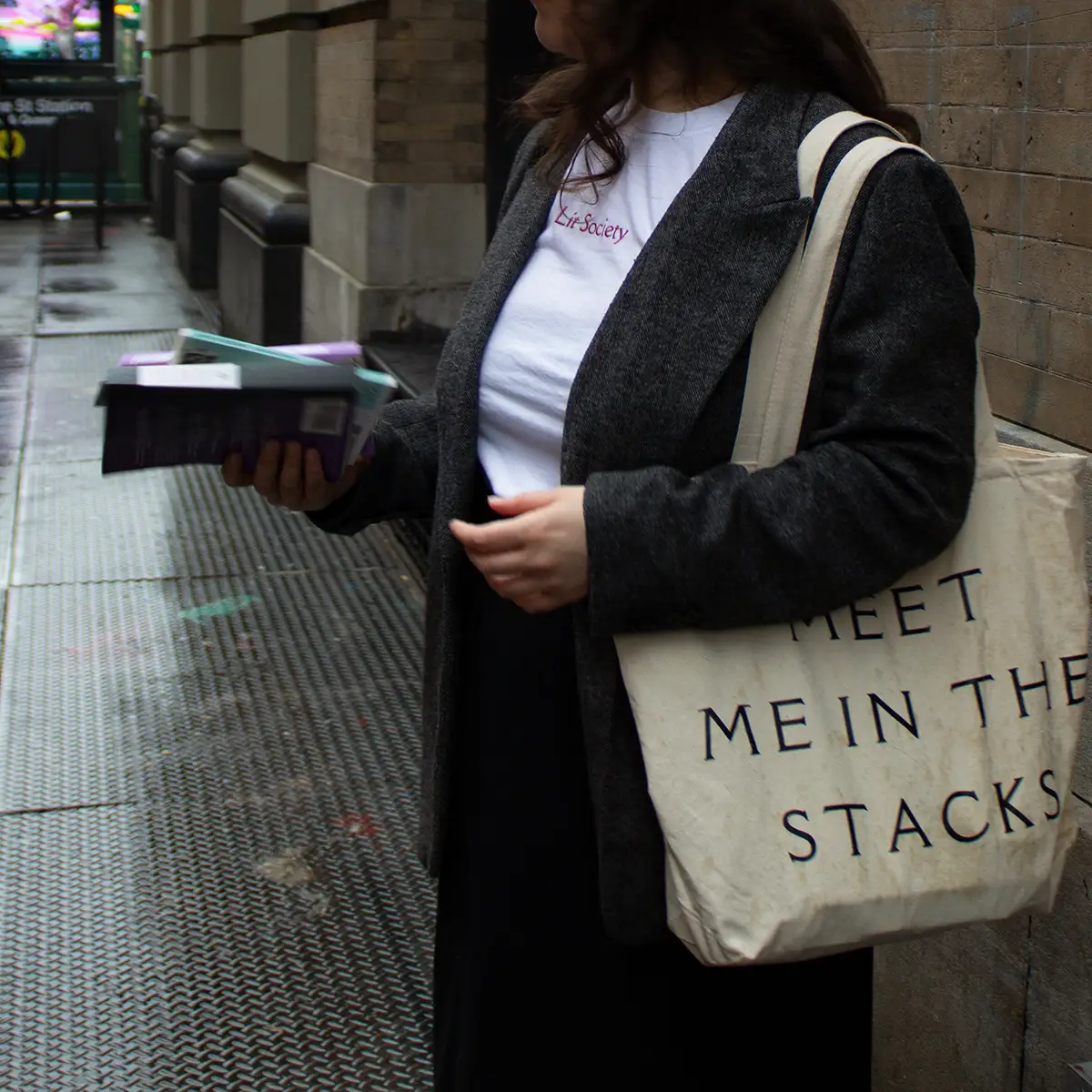 Lit Society member with a "meet me in the stacks" tote bag, holding three books