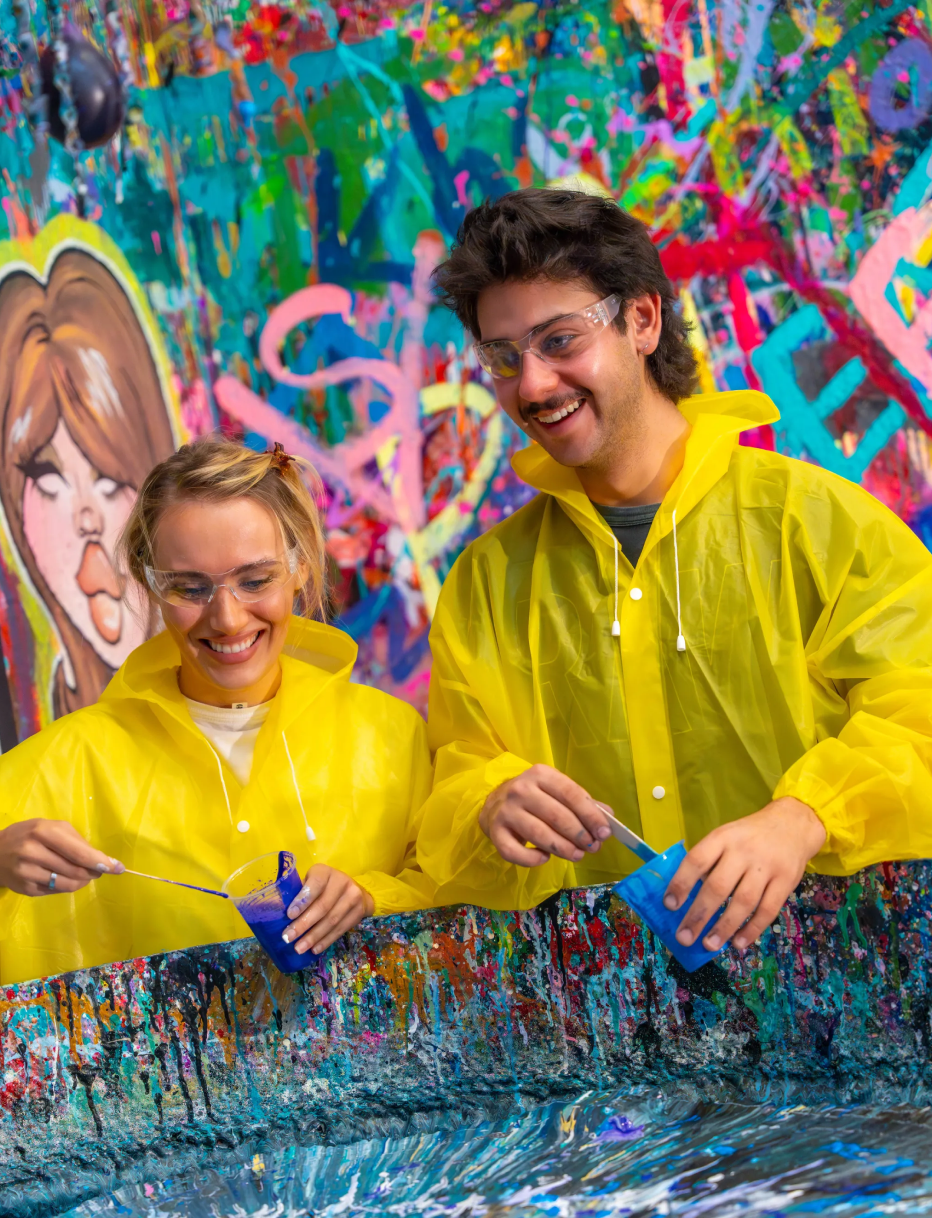 Couple in yellow ponchos pouring blue paint together during date night