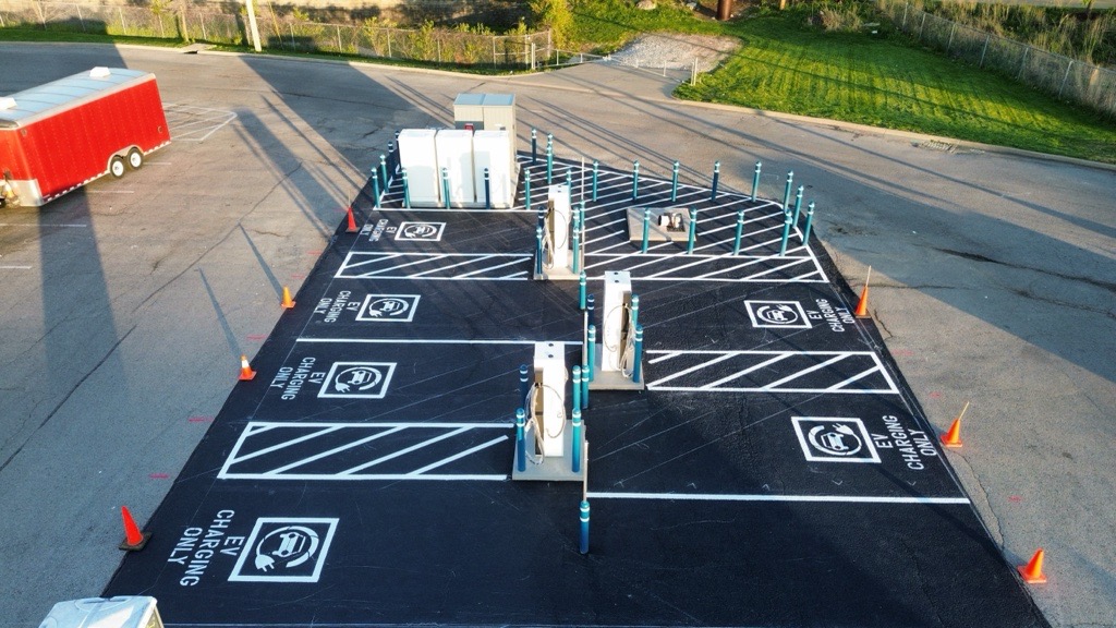 Empty electric vehicle charging station with four parking spaces marked 'EV charging only' and white charging units during daylight.