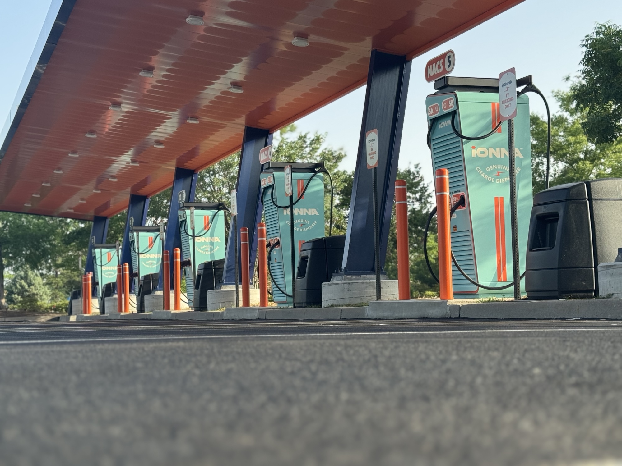 Row of IONNA electric vehicle charging stations under a canopy with trees in the background.