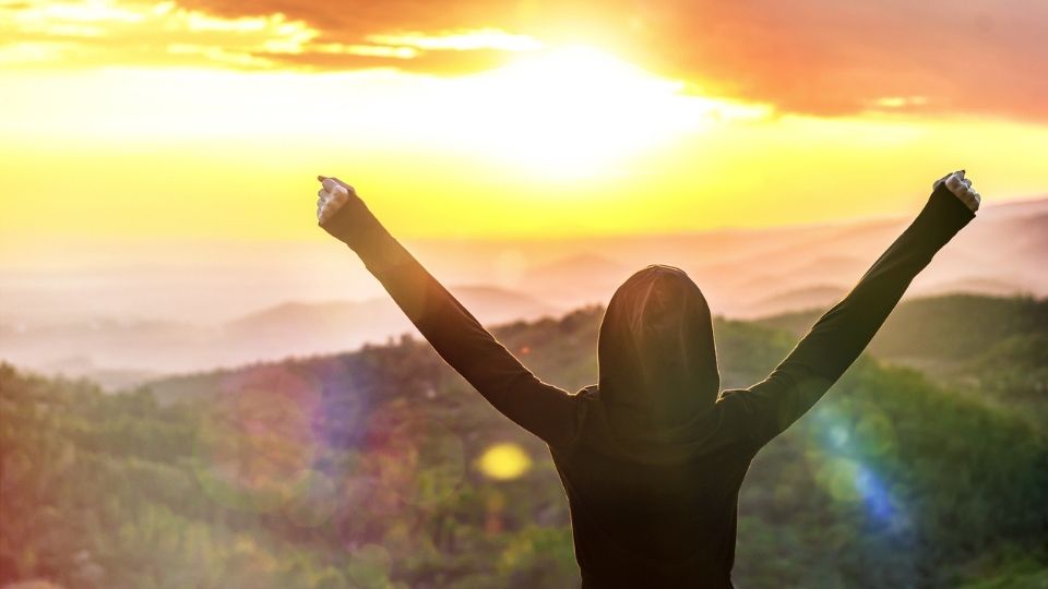 Person with arms raised at sunrise