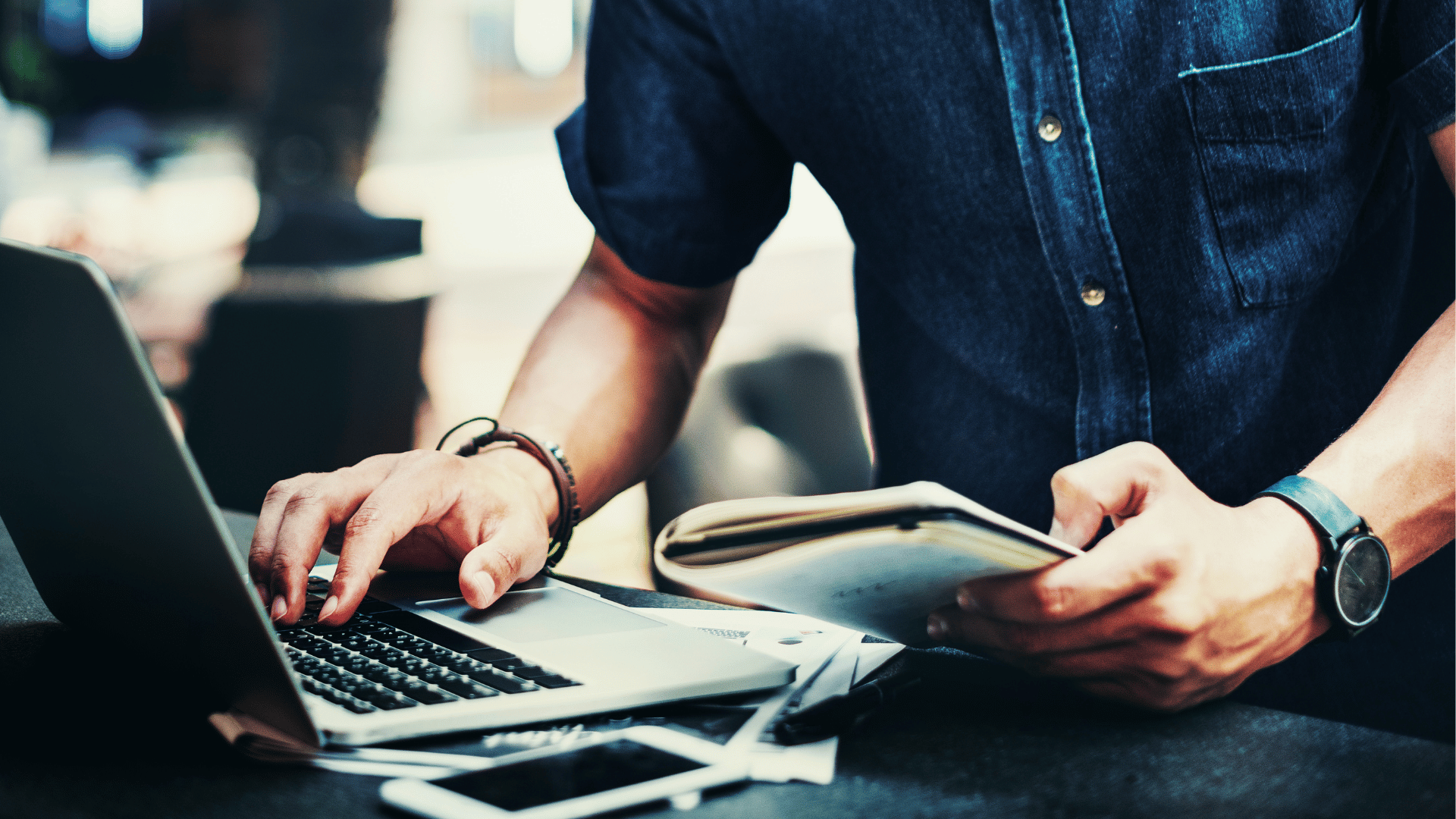 Man in denim shirt keying information into laptop