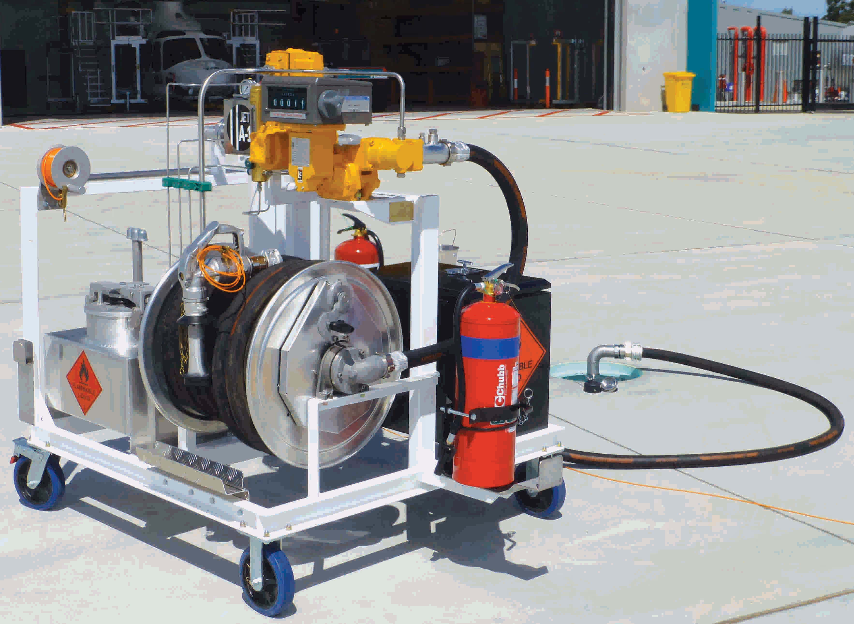 Mobile fuel transfer unit with yellow pump, metal drum, black hoses, and attached red fire extinguisher on a wheeled white metal frame.