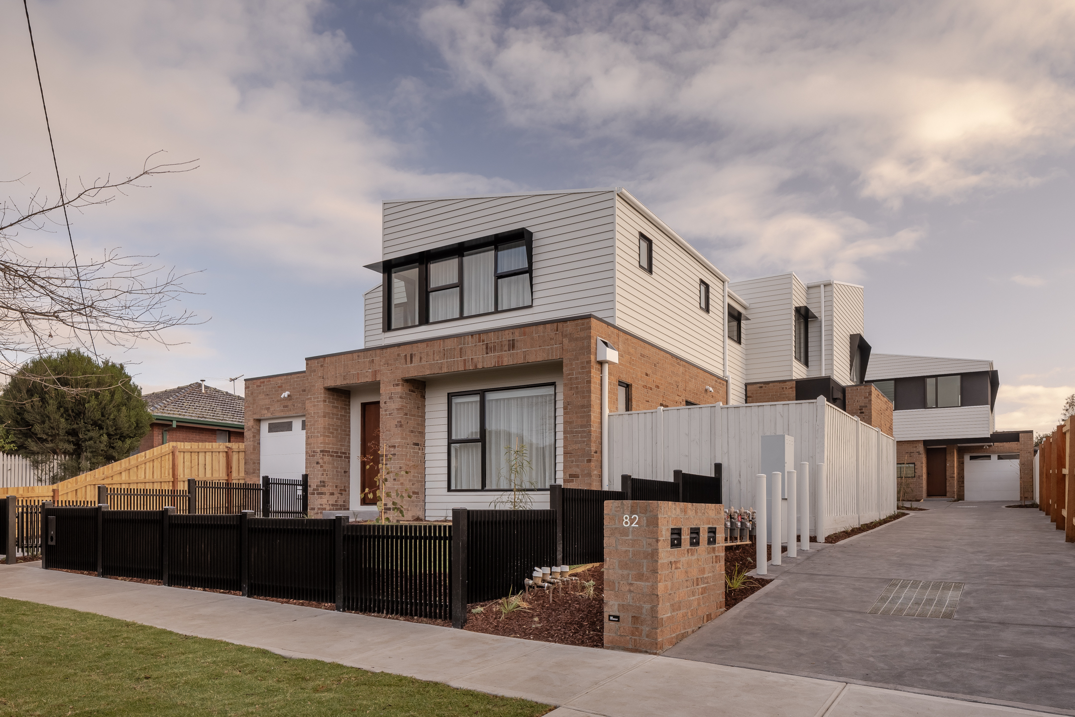 A series of double-storey attached houses with brick work, a garage and black framed windows surrounded by green landscaping
