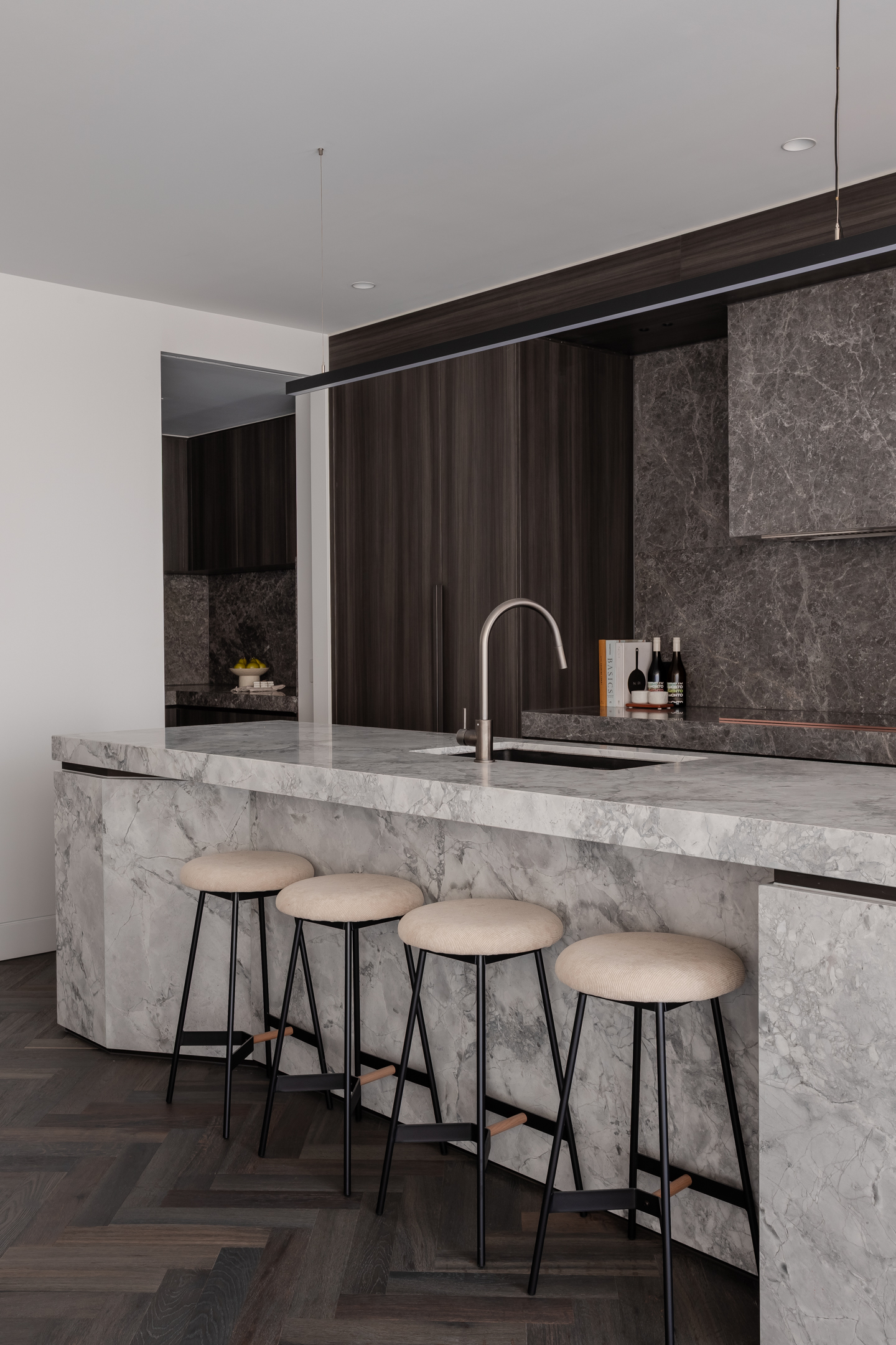 A kitchen with a large marble island, fresh produce and kitchenware neatly arranged on the countertop, floor-to-ceiling windows.