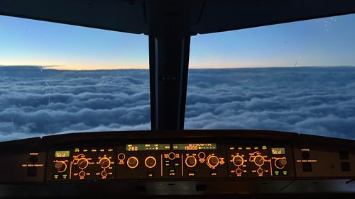 View from the cockpit with dials in the foreground. Clouds and a sunset are visible through the pilots windows.