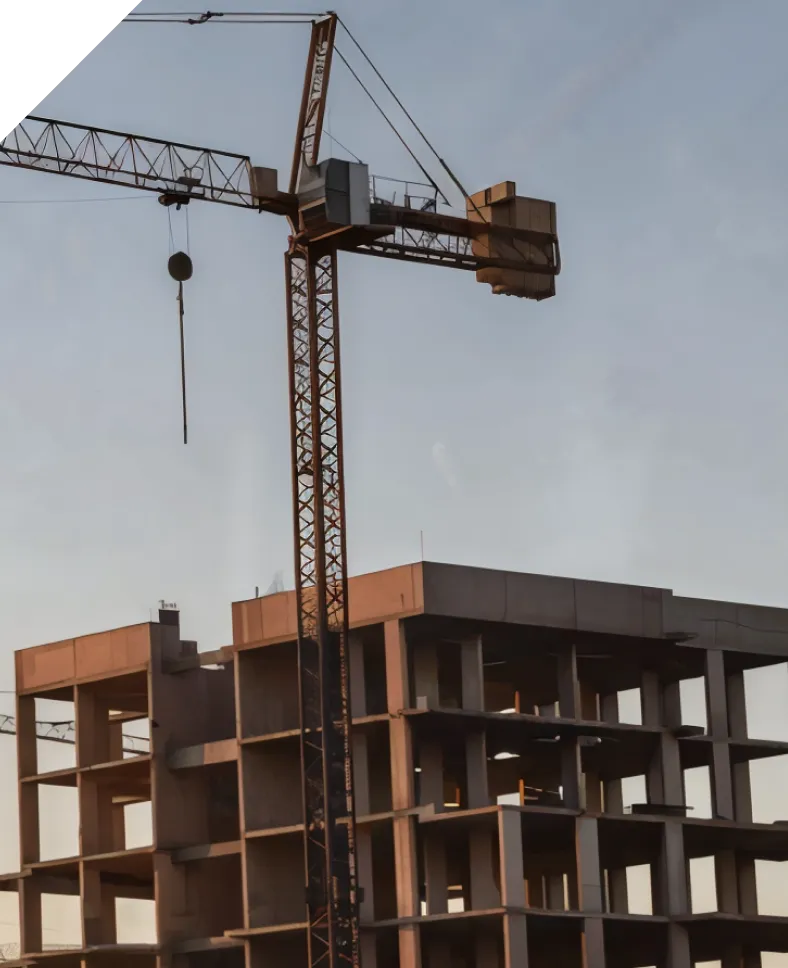 Будівельний кран біля незавершеного багатоповерхового будинку серед густого хвойного лісу.