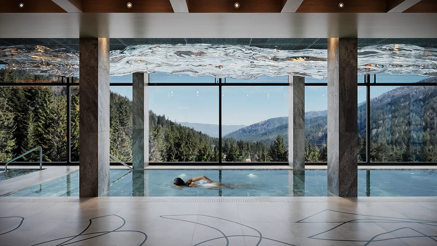 Жінка плаває в критому басейні з великими вікнами, що відкривають вид на лісисті гори.