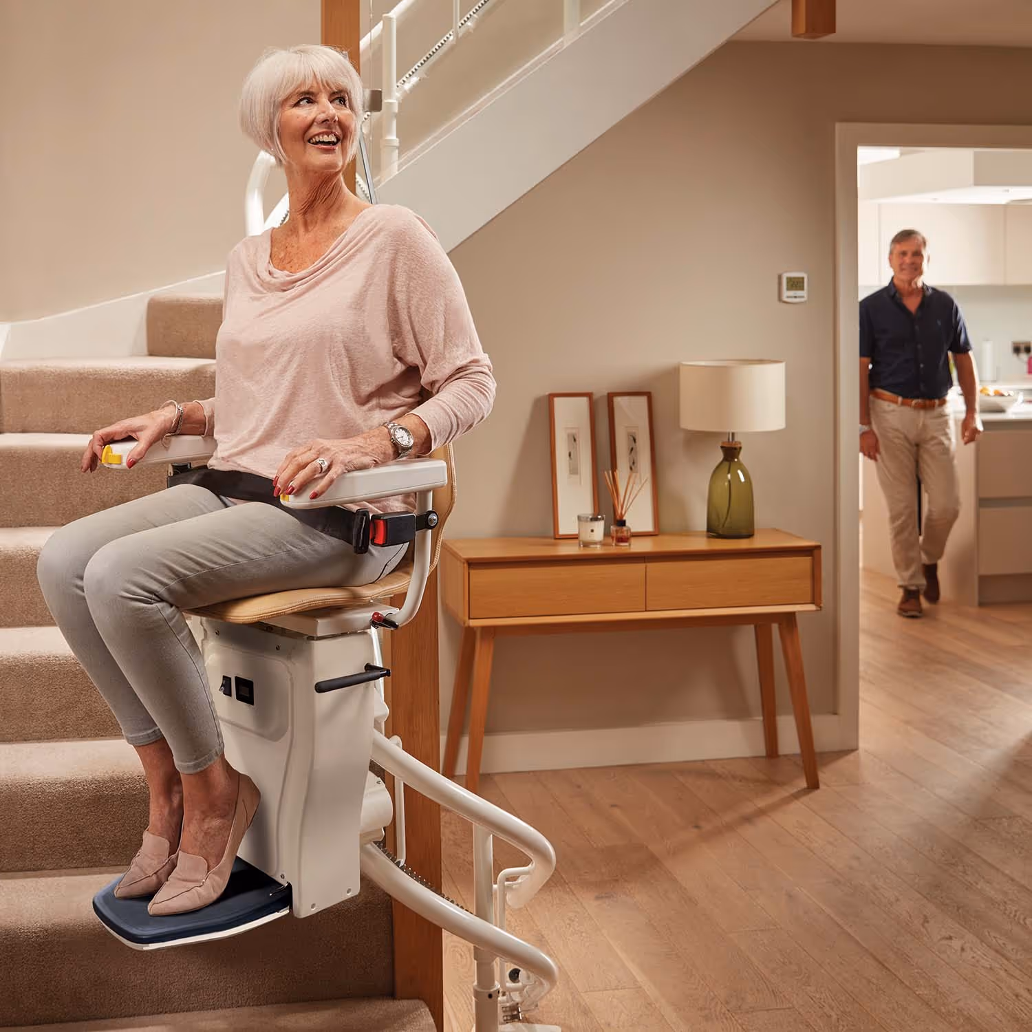Senior woman using stairlift at home while a man stands in the background