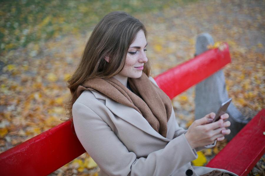 Woman on bench in beige coat holding smartphone