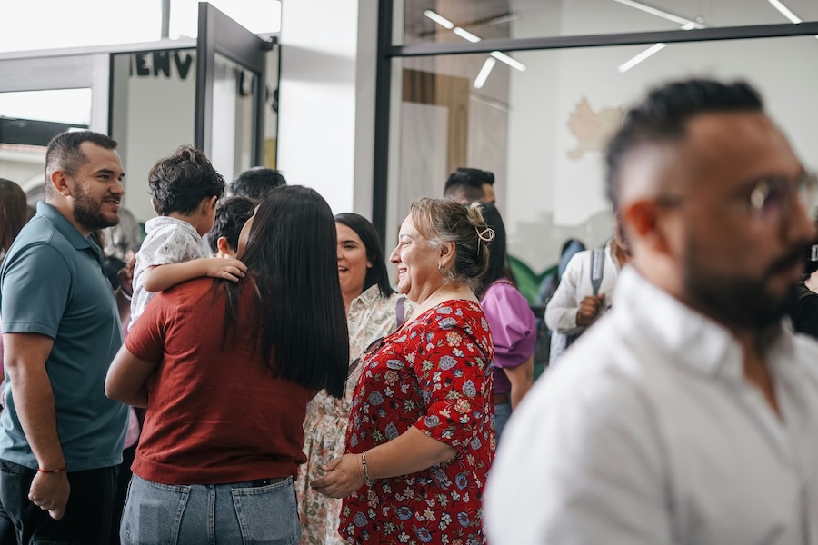 People chatting and smiling in a bright church foyer after a service, with adults and a child gathered informally near glass doors.
