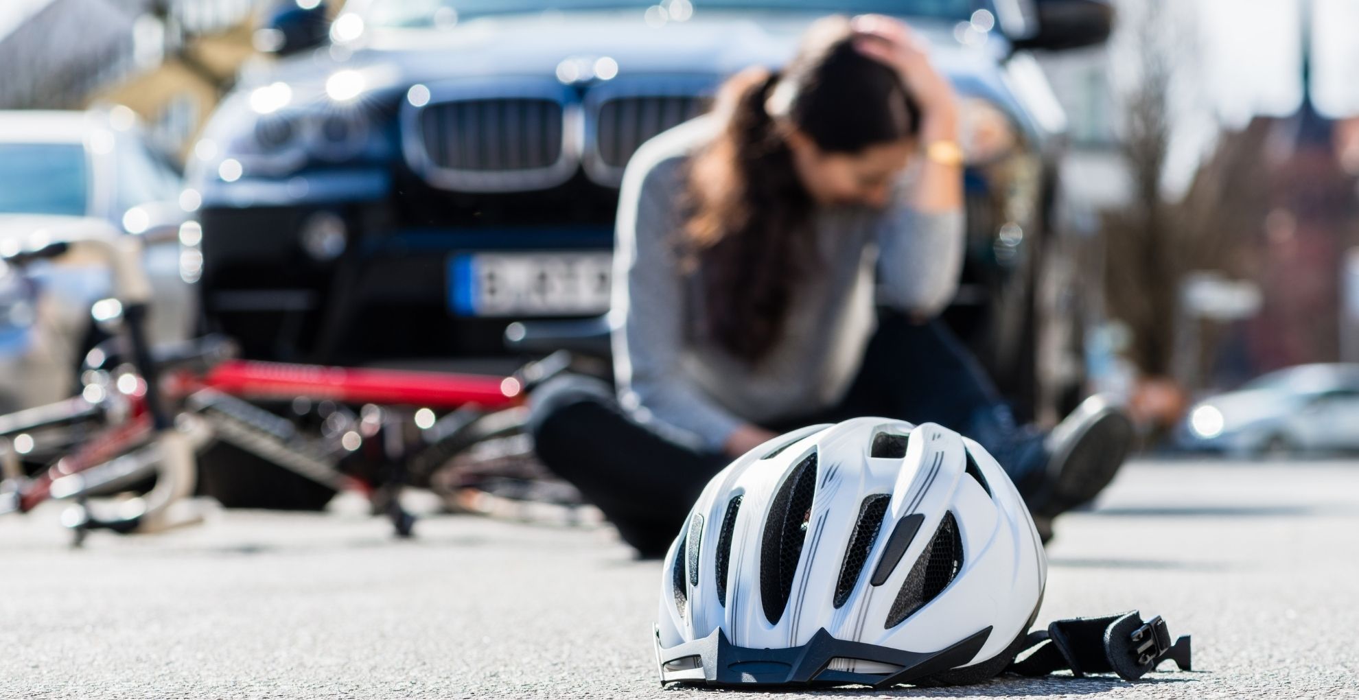 Fietshelm op straat met zittende vrouw op achtergrond die hoofd vasthoudt en auto.