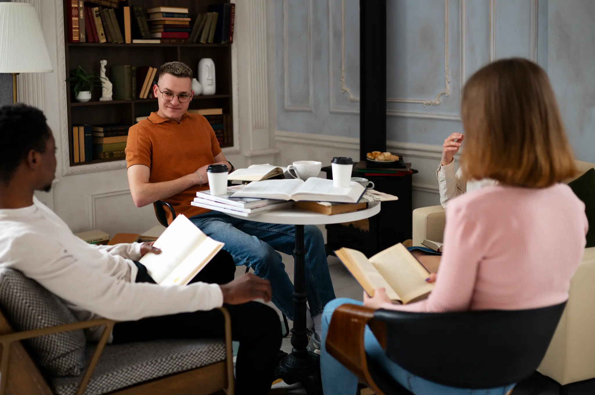 StoryTerrace - Books That Matter - Three people reading books and drinking coffee in a cozy room.