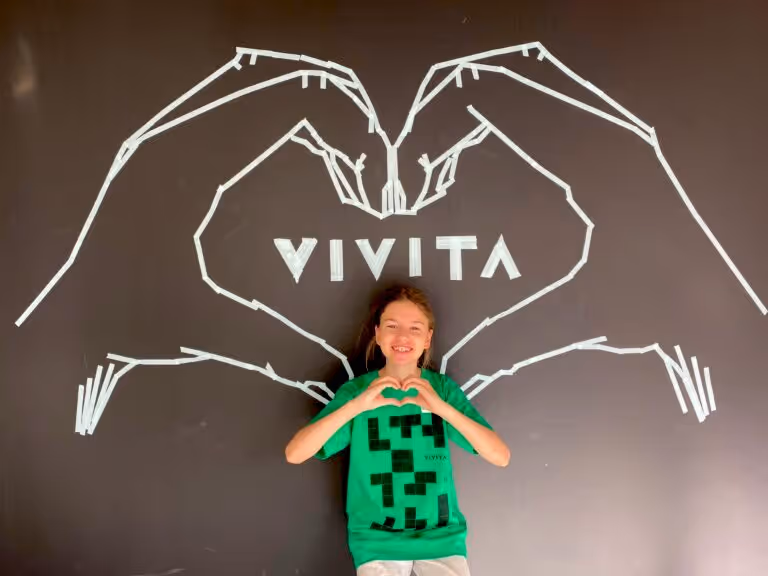 A kid showing heart with hand gestures and standing in front of Vivita logo