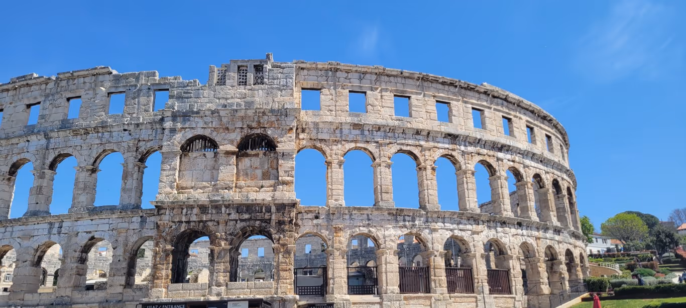The old Roman amphitheater in Pula, a great day trip from Trieste, against a bright blue sky.