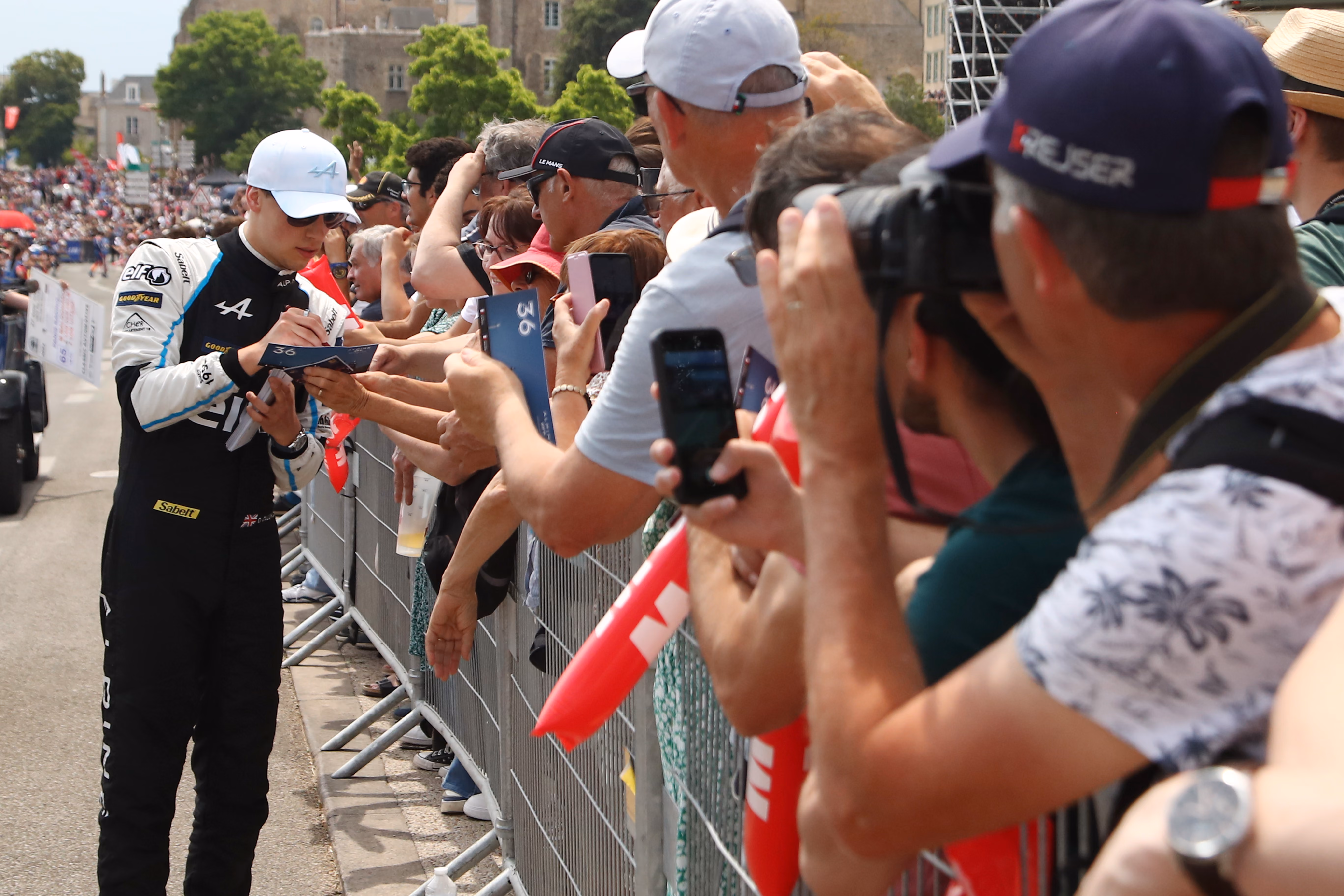 Racing driver signing autographs for fans behind a metal barrier.