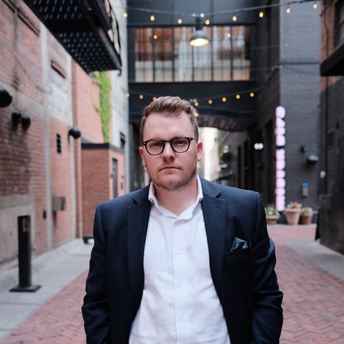 A man in a suit and glasses standing on a brick sidewalk.