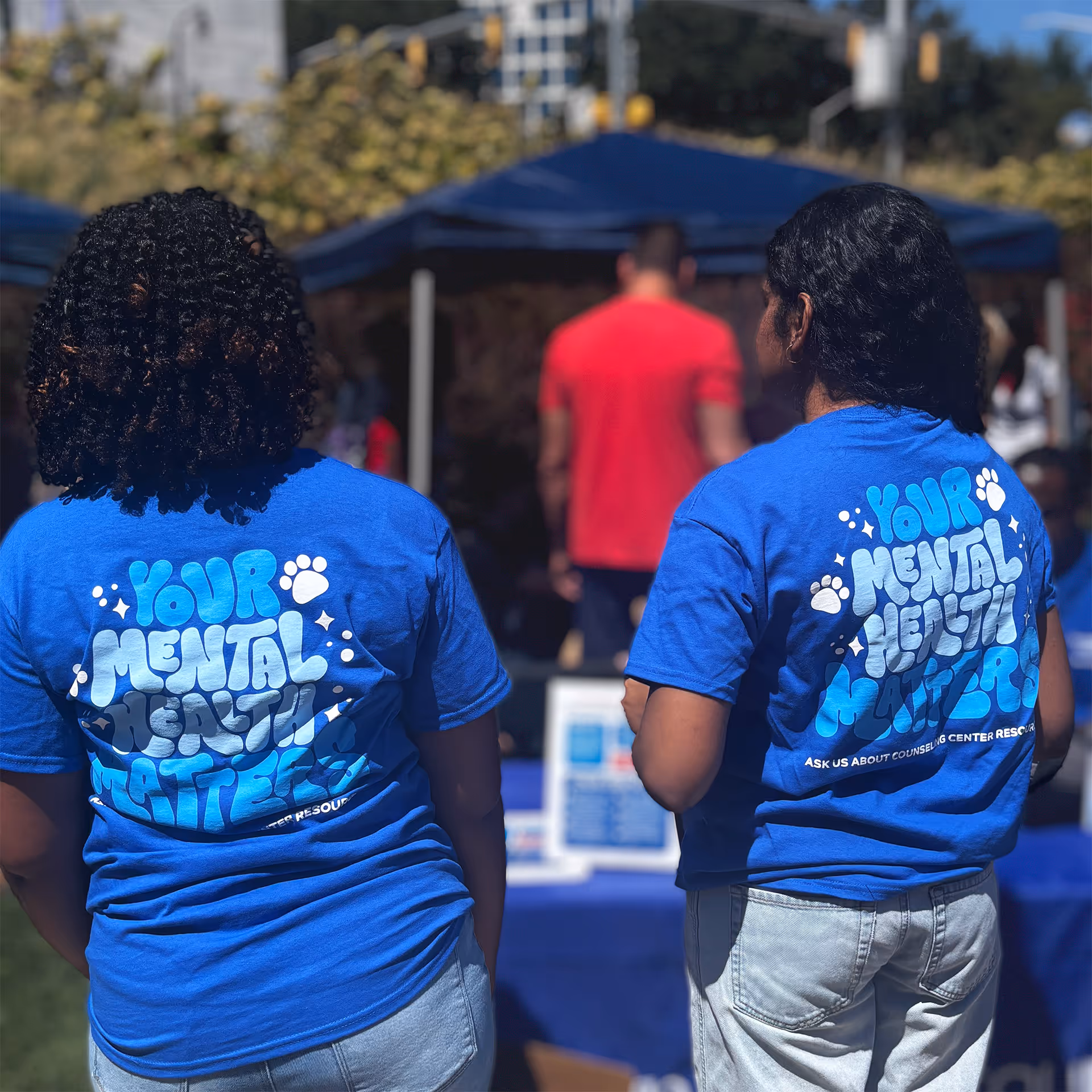 Two people wearing blue shirts reading 'Your mental health matters' at an outdoor event booth.