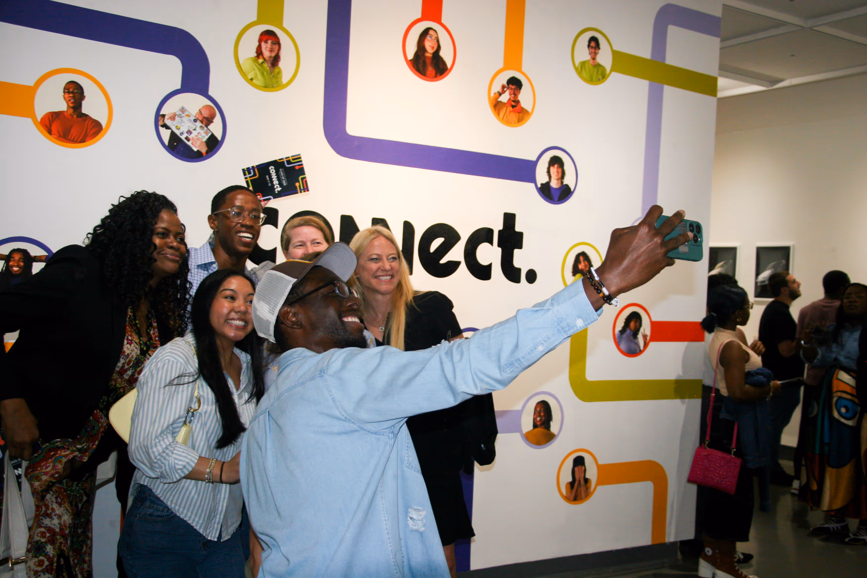 Group of people smiling and posing for a selfie in front of a colorful wall that says Connect.