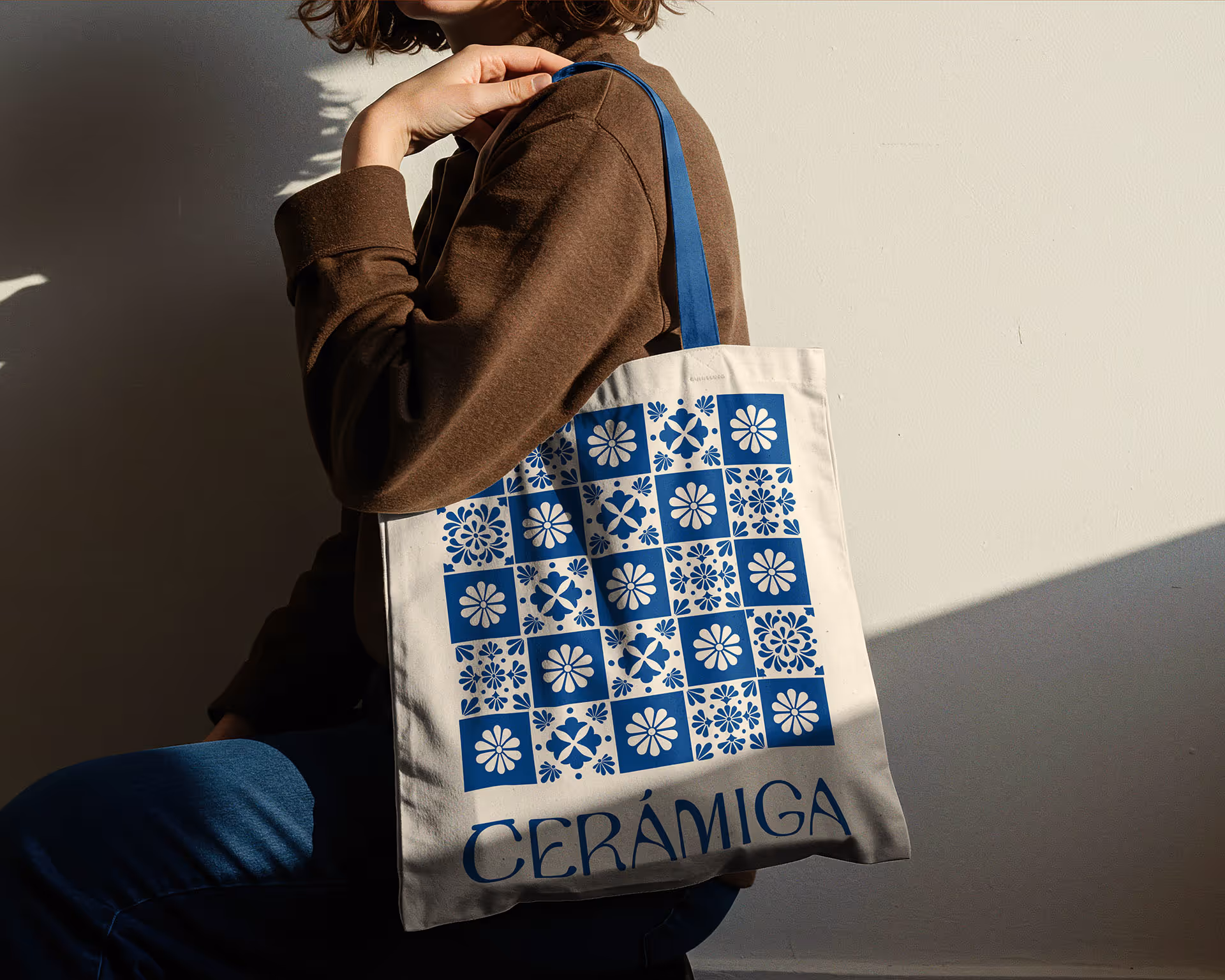 Person holding beige tote bag with blue floral square patterns and the word CERÁMIGA.
