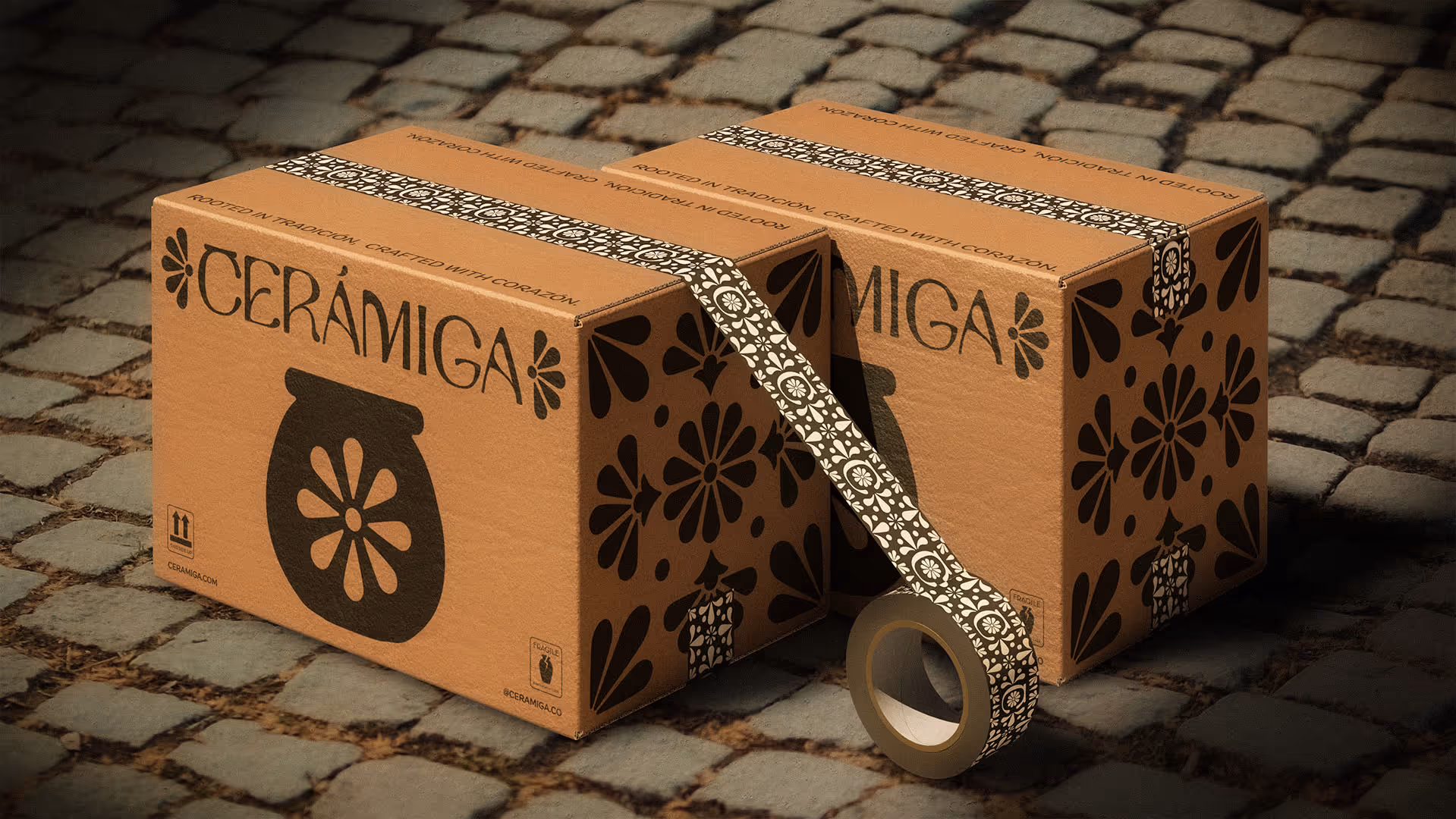 Two brown cardboard shipping boxes with black floral designs and the brand name CERÁMIGA on cobblestone ground.
