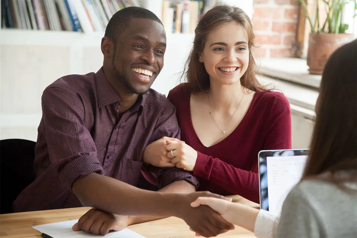 A couple shaking hands with a financial advisor for helping them refinance their home loan.