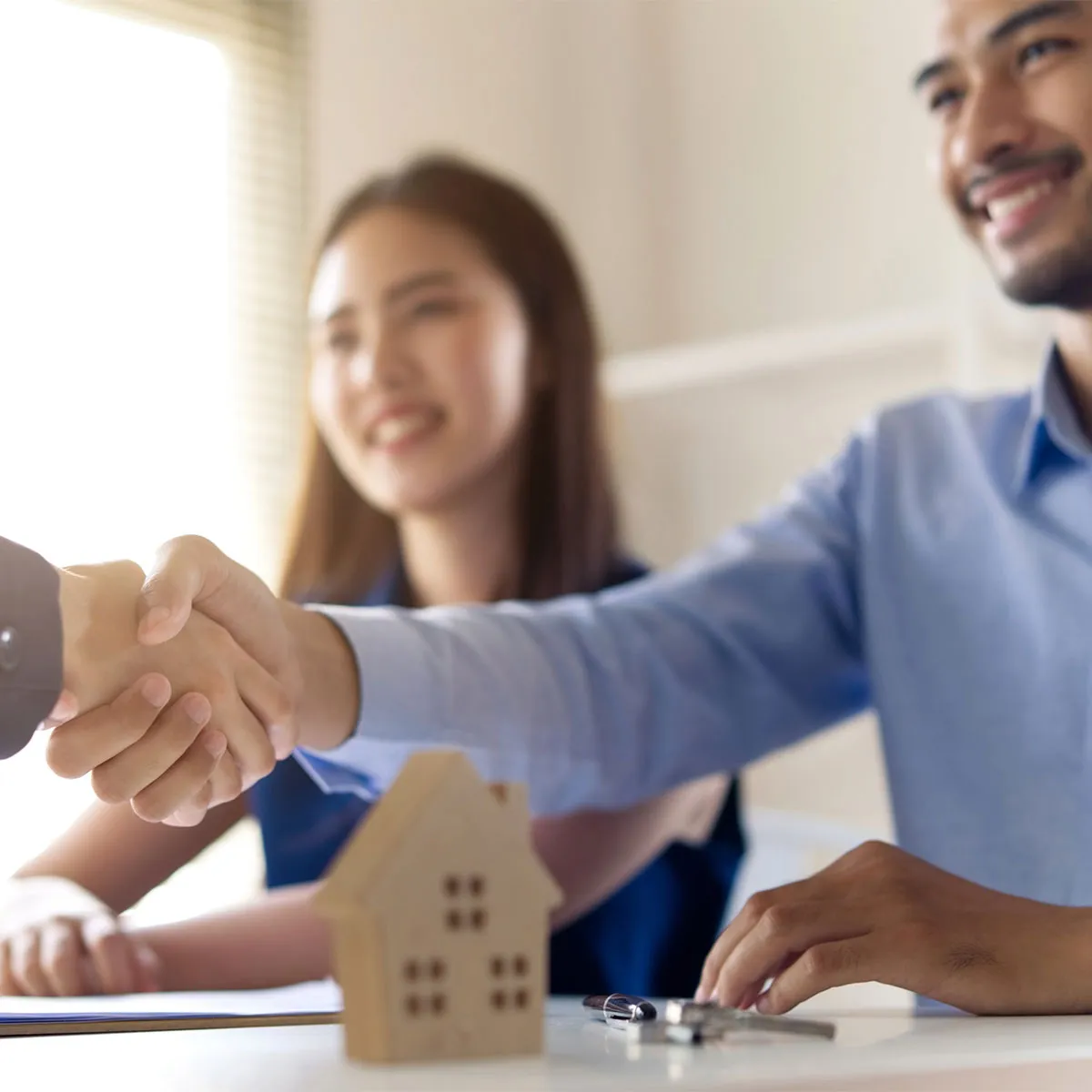A couple shaking hands with a financial advisor and smiling because they have refinanced their home loan.